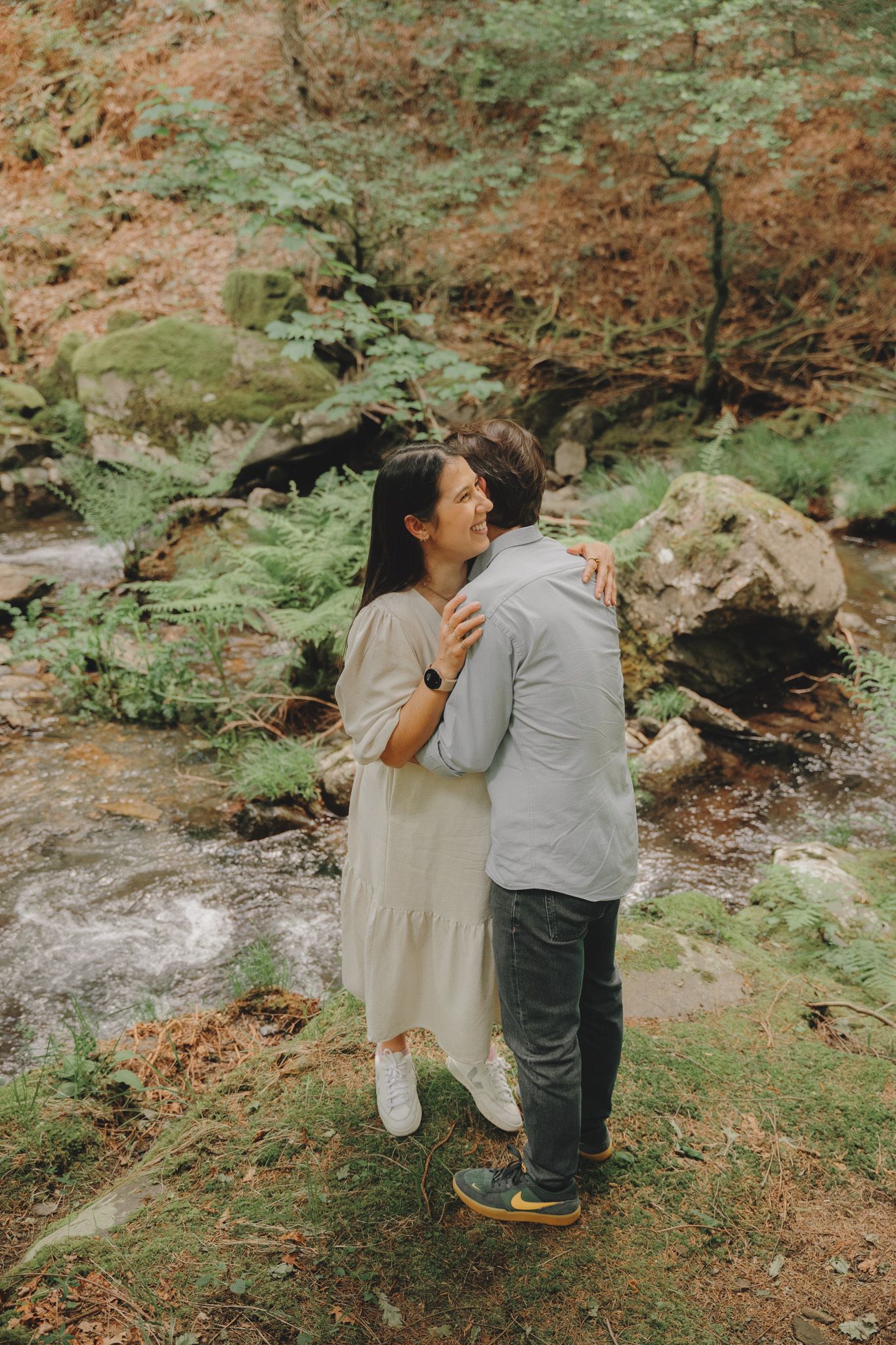 A romantic sequence of a couple sitting together on mossy rocks in a forest.