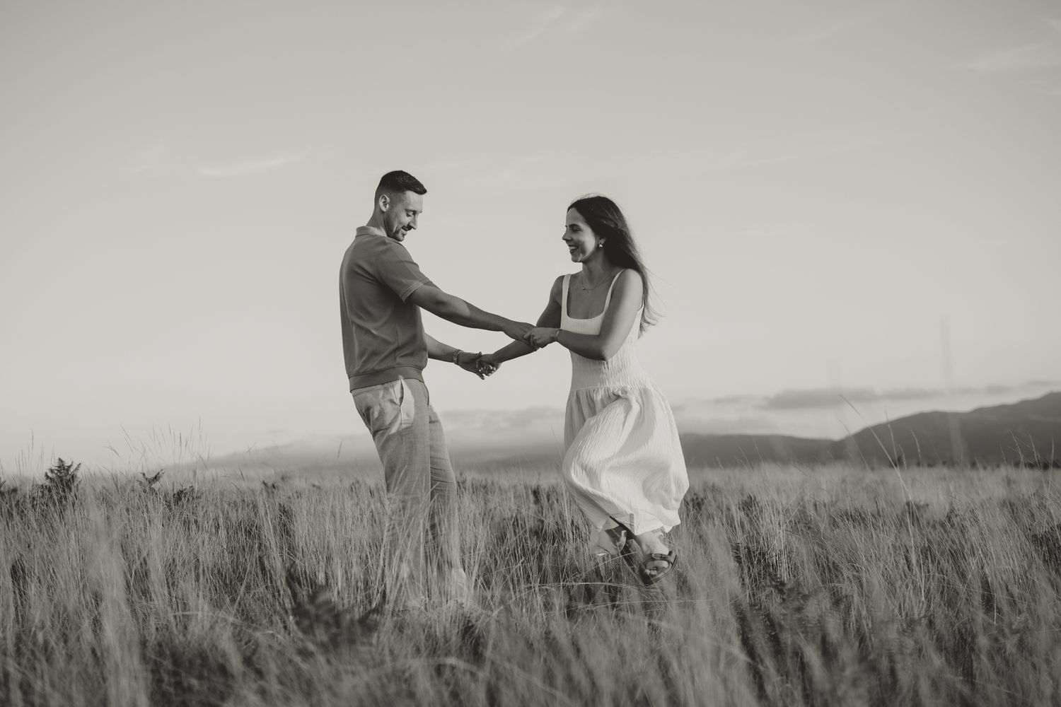 A couple holds hands while walking through a misty field in black and white.