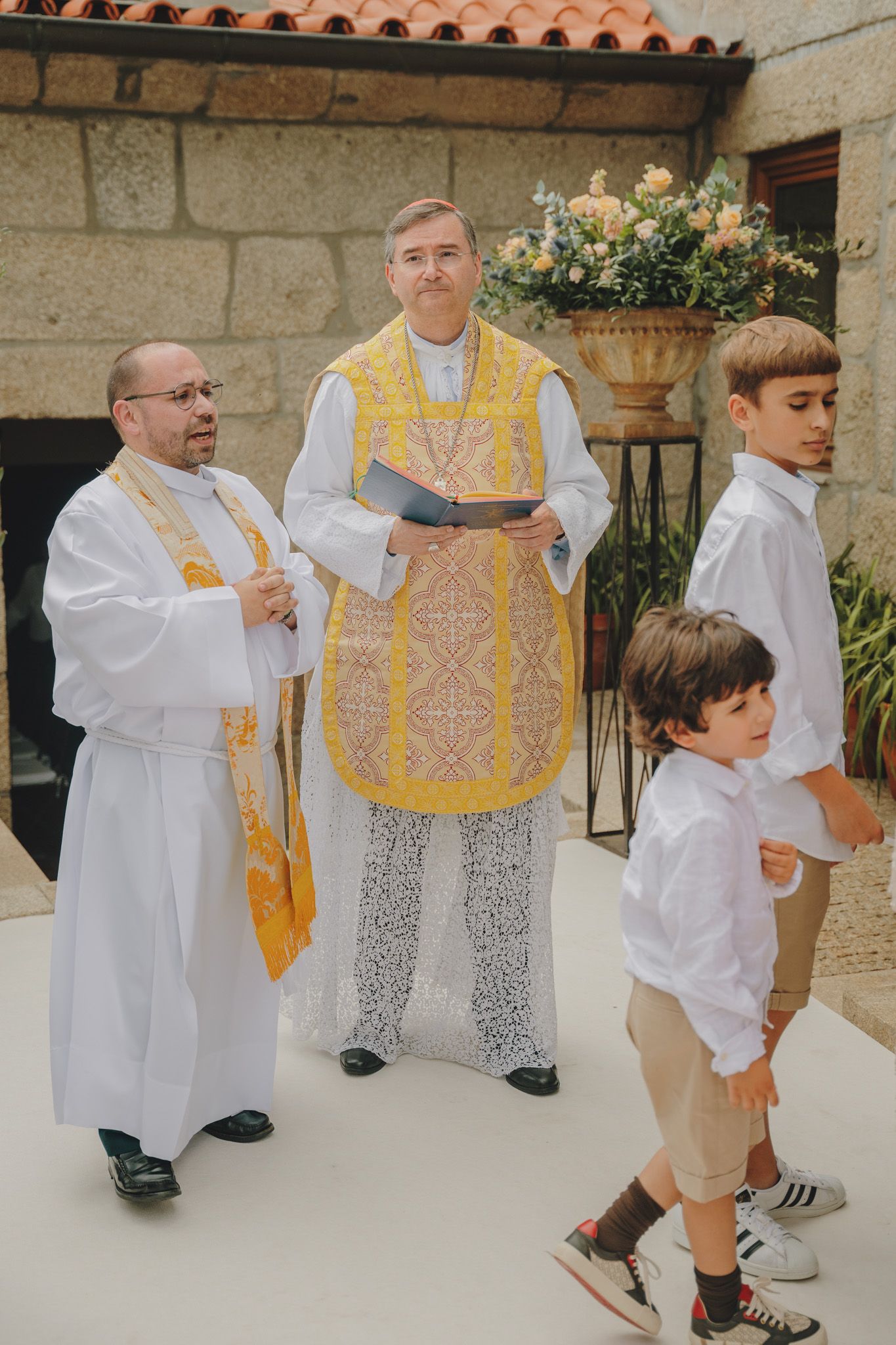 Young ring bearers in white shirts walk alongside clergy members in gold vestments.