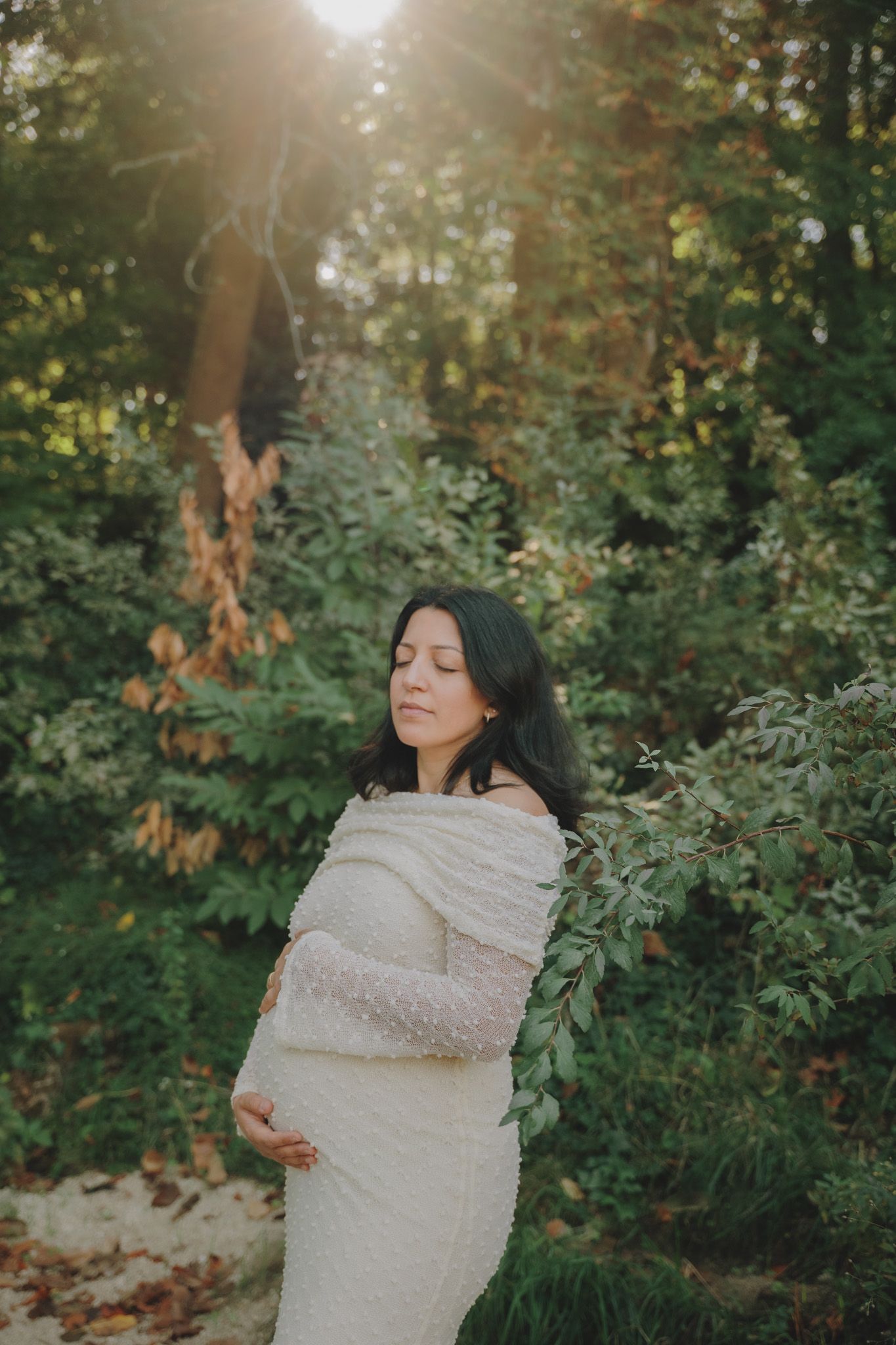 Woman in cream dress poses in sunlit garden with autumn foliage.