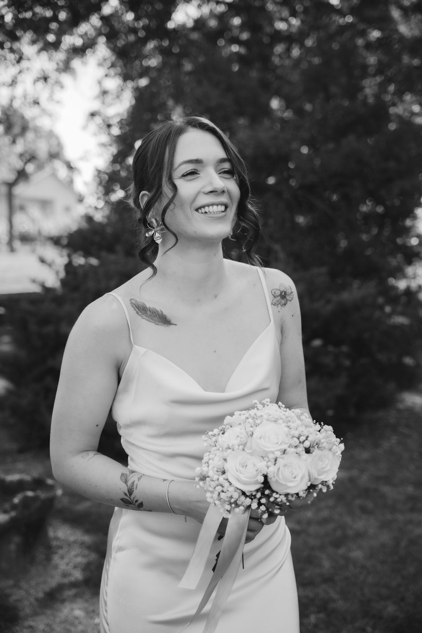 Black and white portrait of joyful bride holding white bouquet in garden setting.