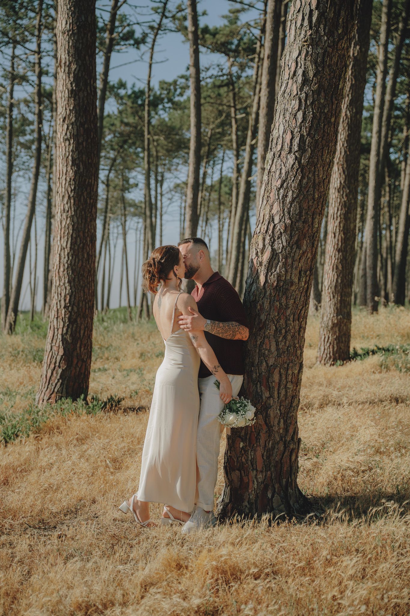 Intimate moment between newlyweds among tall pine trees in golden light.