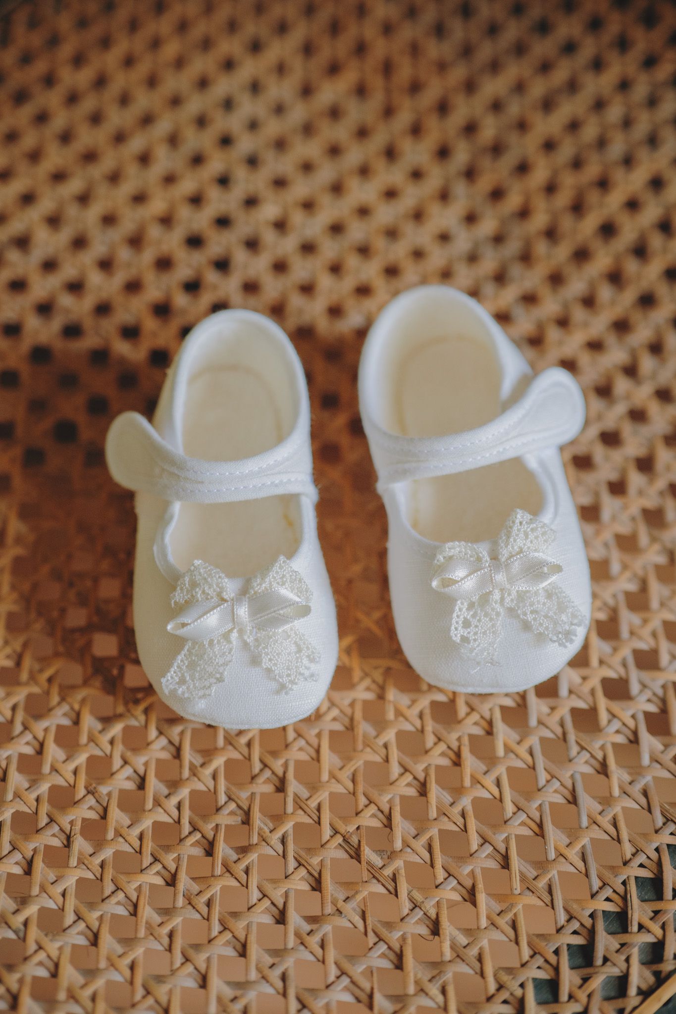 Tiny white baby booties with lace details on a woven textured surface.