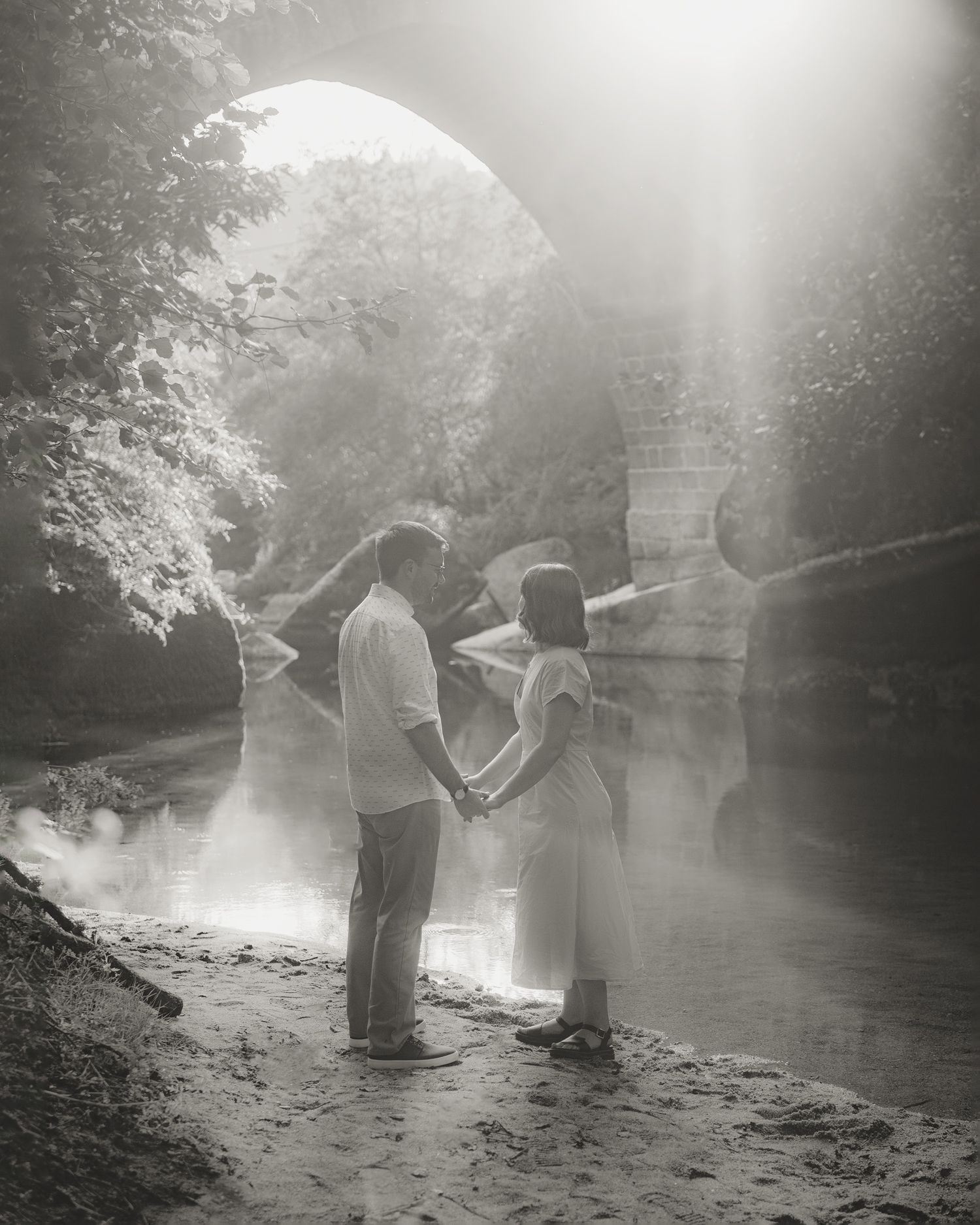 Dreamy black and white photo of figures by a misty river at sunset.