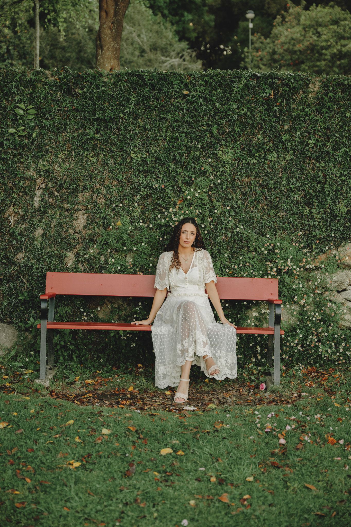 White lace dress against a backdrop of green foliage and a red bench in a garden setting.