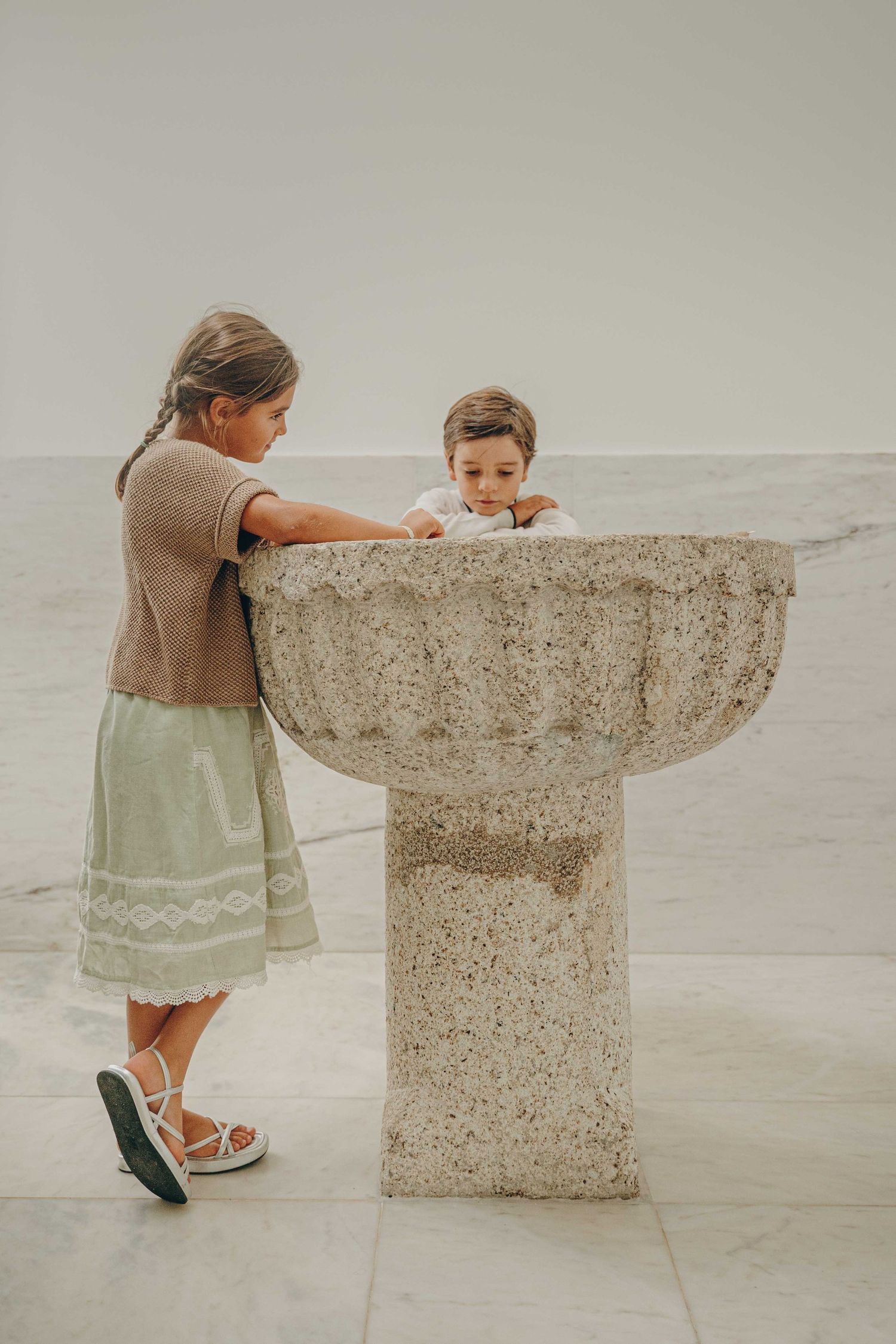 A child explores a modern concrete water fountain from different angles in a minimalist setting.