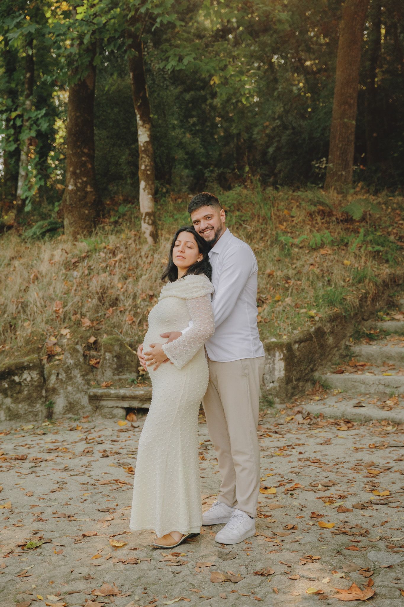 A sunlit maternity portrait in a forest setting with autumn foliage.