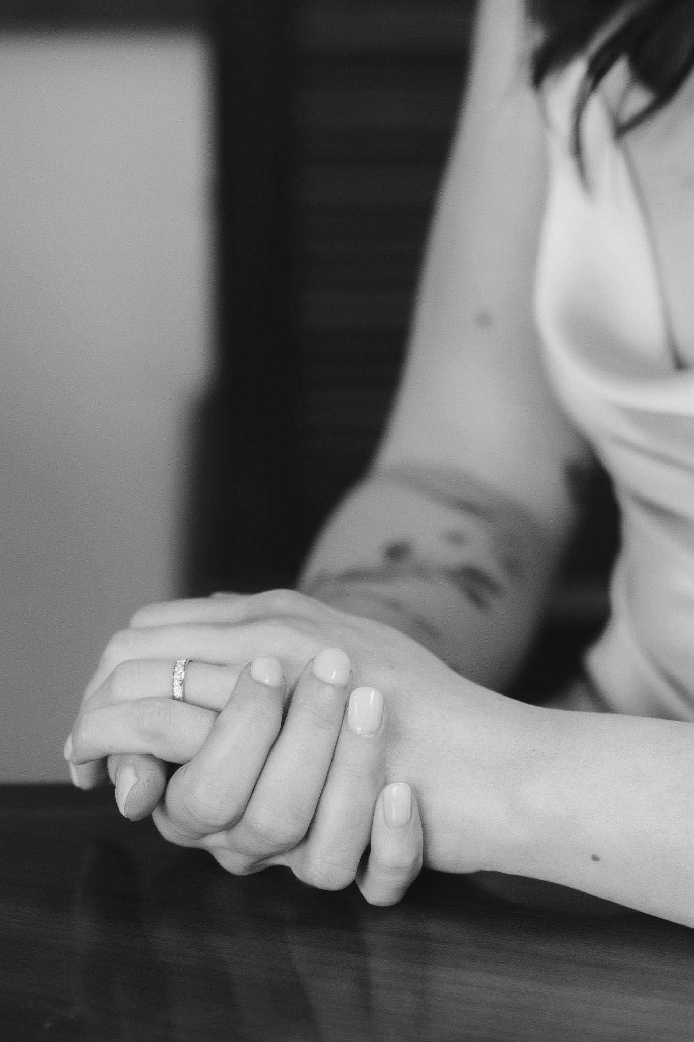 Close-up black and white photo of clasped hands with a wedding ring.