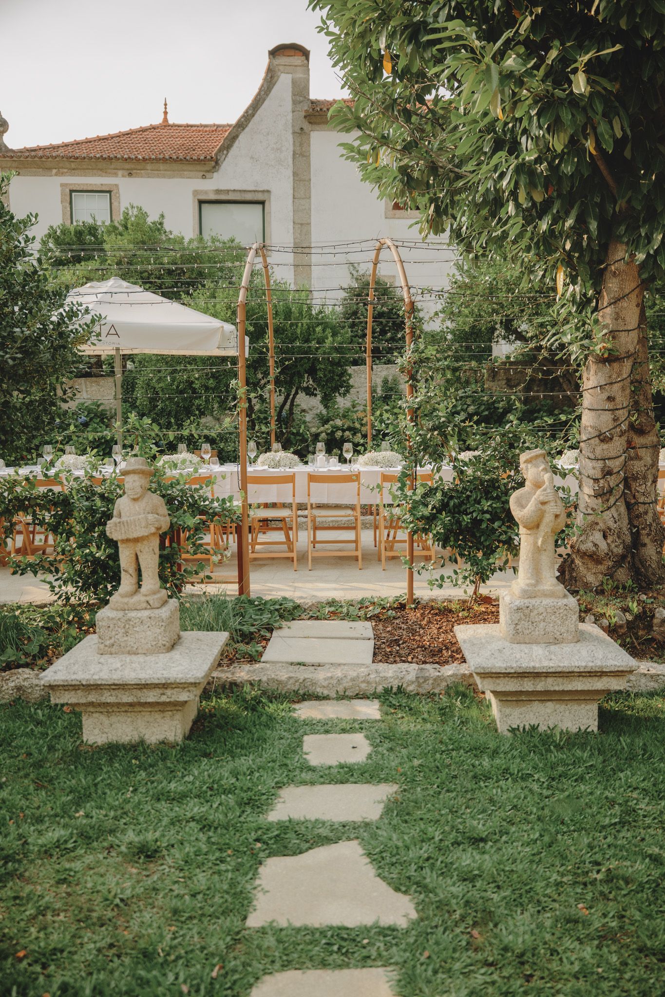 Stone pillars line a garden path with wooden pergola and greenery.
