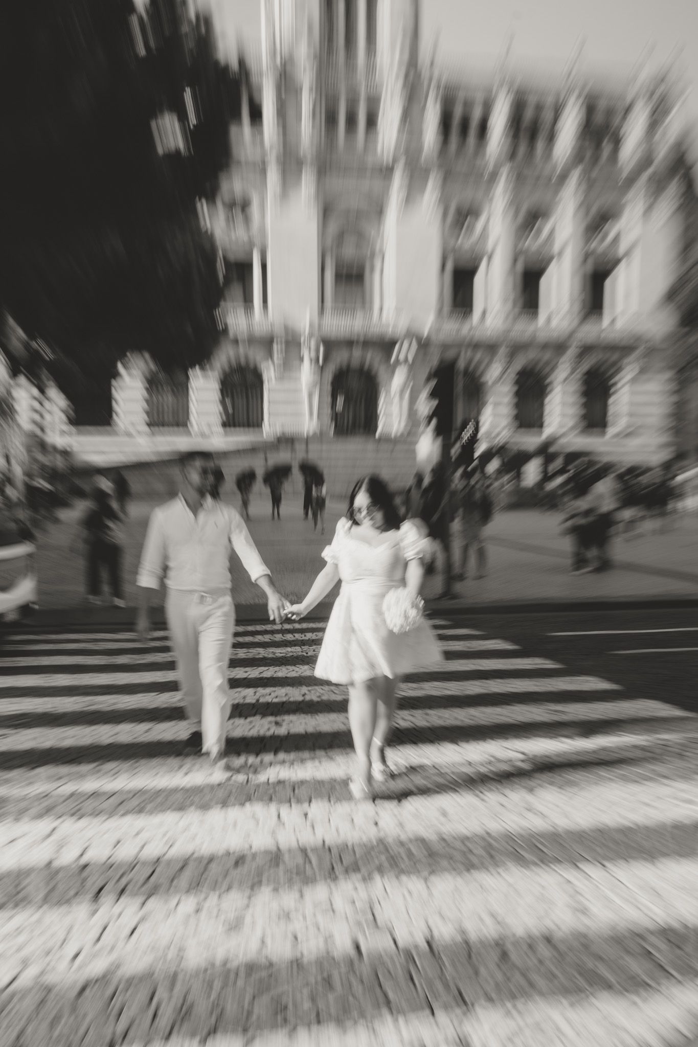 Two people in white clothing walking along a blurred urban sidewalk in black and white.