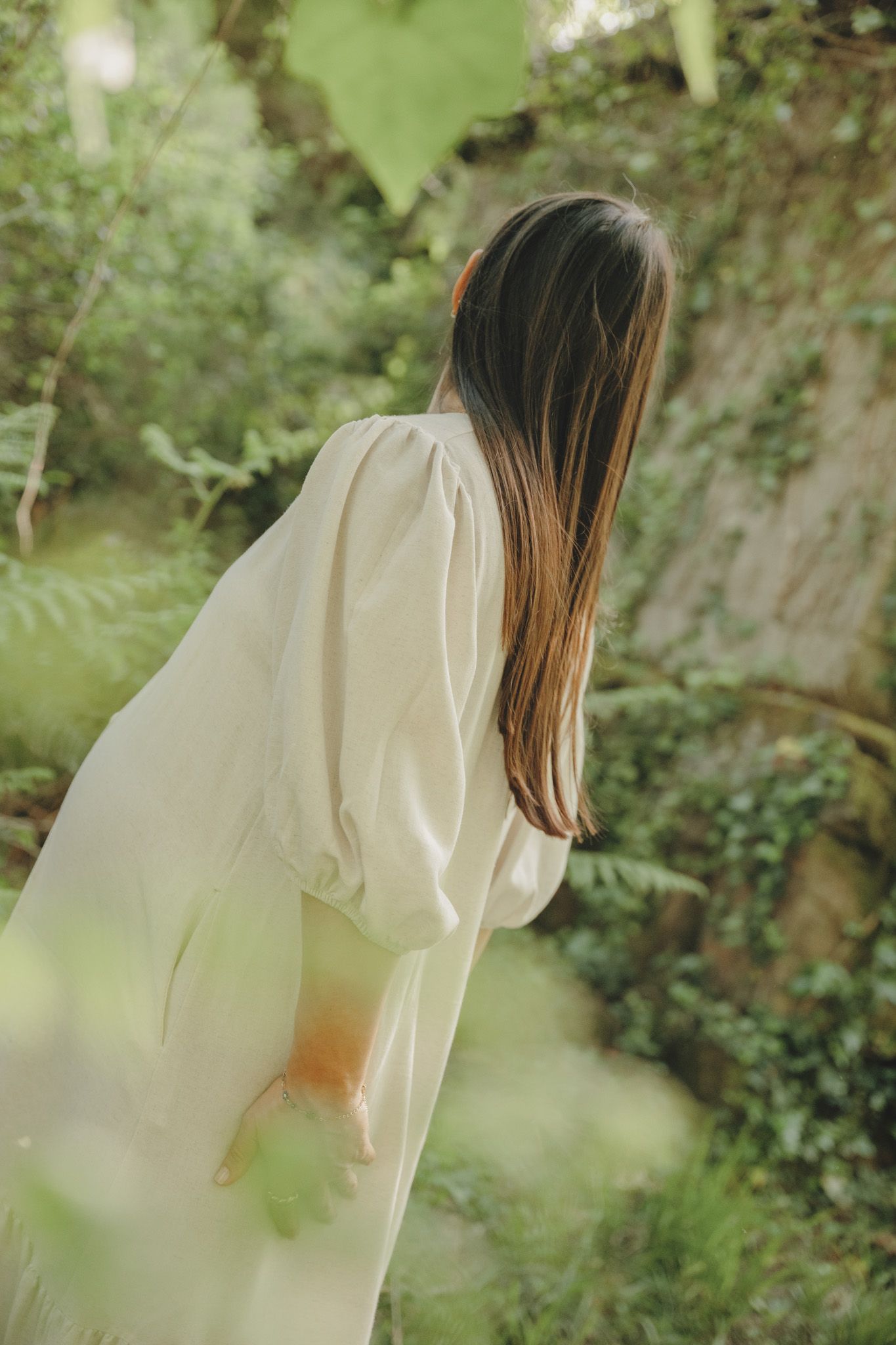 A person in a white dress walks through a lush green garden setting creating a dreamy ethereal atmosphere.