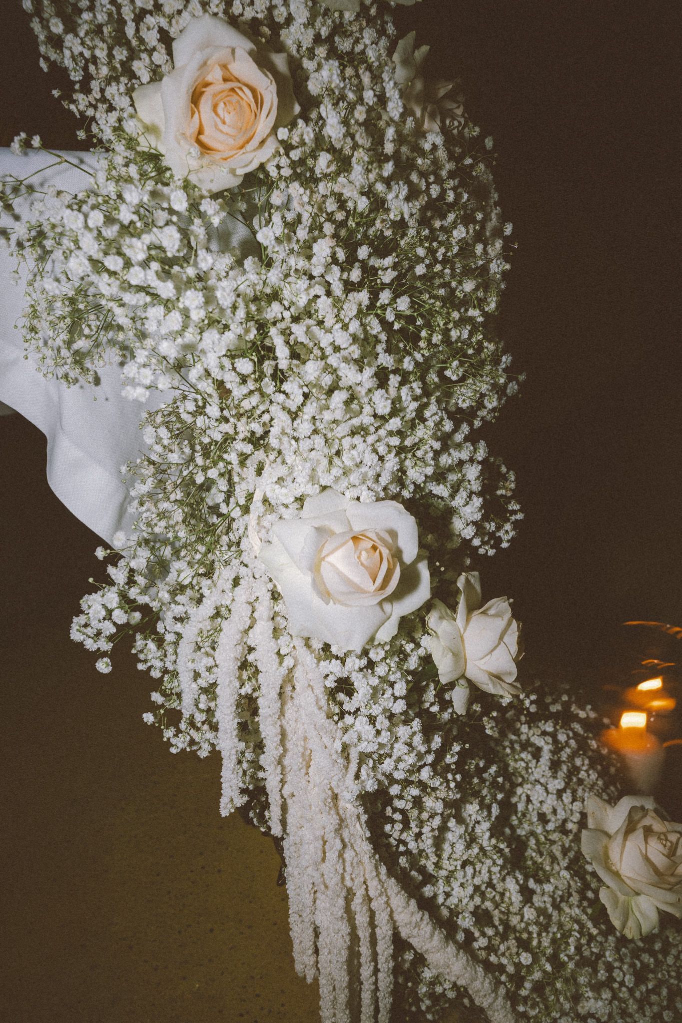 Elegant floral arrangement with white roses and baby's breath against a dark background.