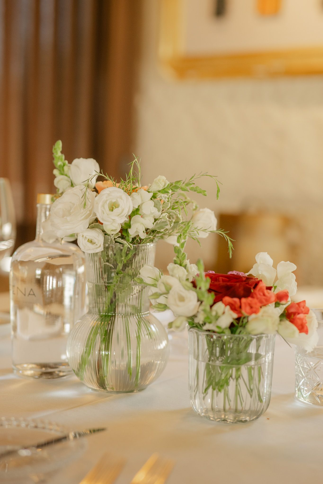 Glass vases with delicate white and coral flowers on wedding reception table.