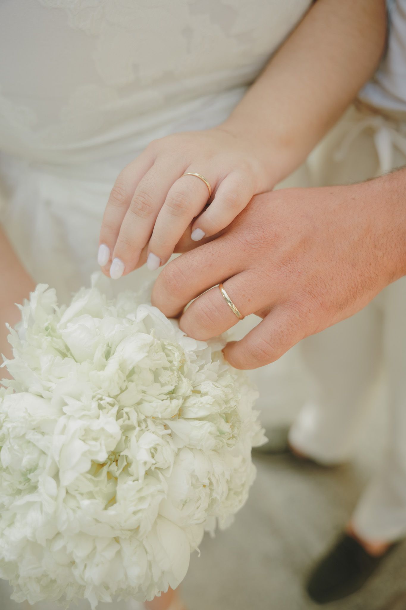 Close-up of hands delicately touching white flowers in a wedding bouquet.