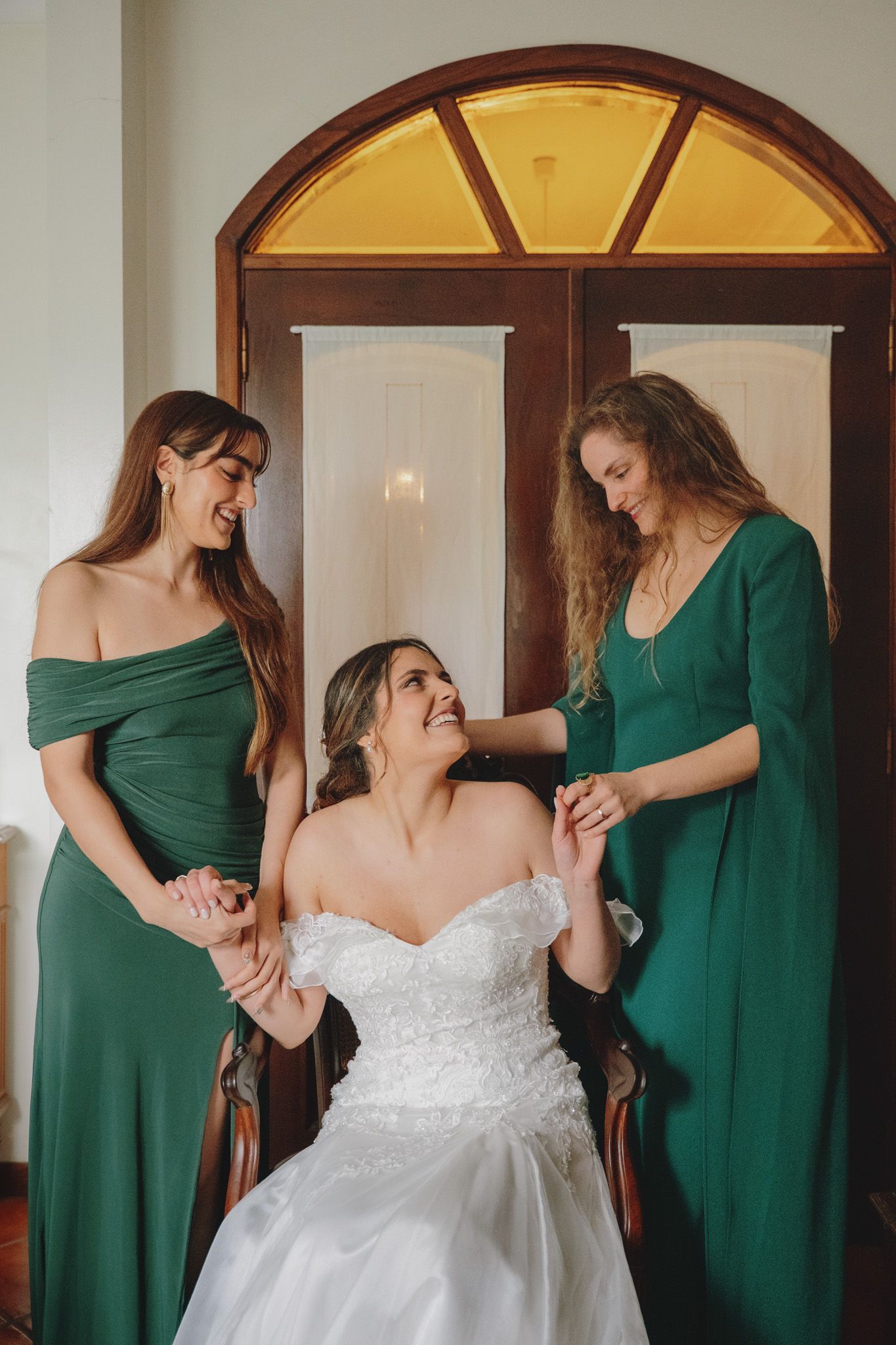 Wedding party wearing emerald green dresses helping with final dress preparations.