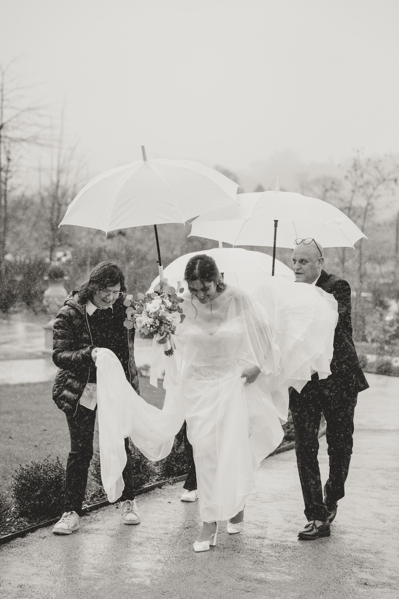 Wedding party runs through the rain holding white umbrellas in a playful moment.