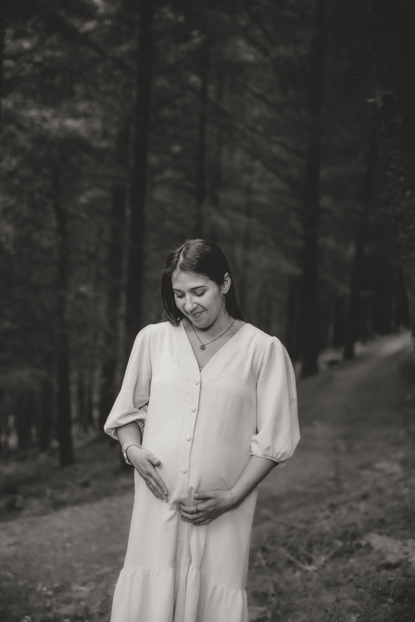 A black and white photo of someone in a white dress standing in a wooded setting.