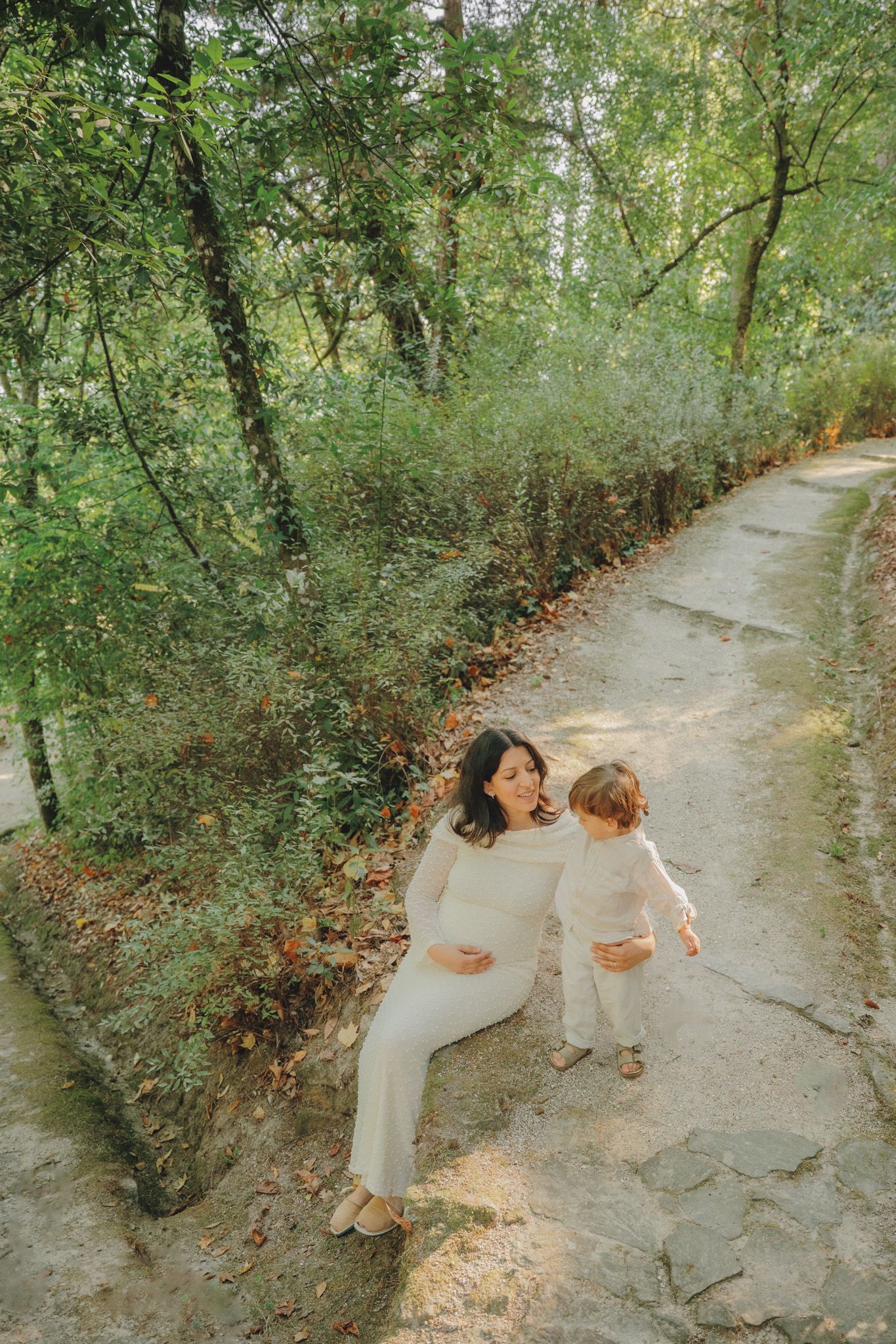 Two figures in white outfits sit together on a winding forest path.
