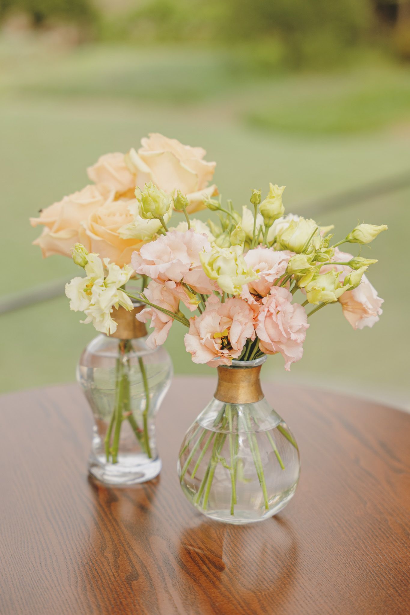 Delicate peach and pink flowers arranged in clear glass vases on a wooden table.