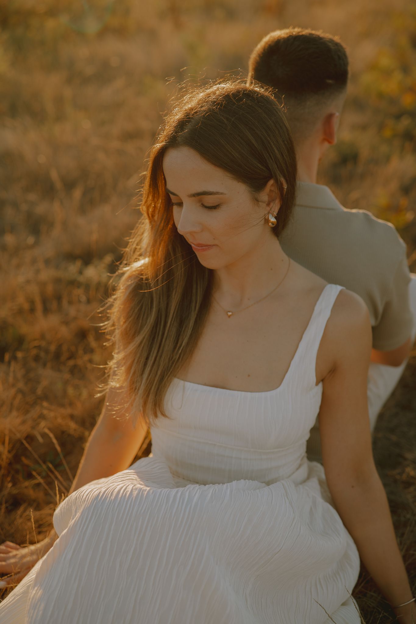 Warm sunset light illuminates a couple in a field with golden tones.
