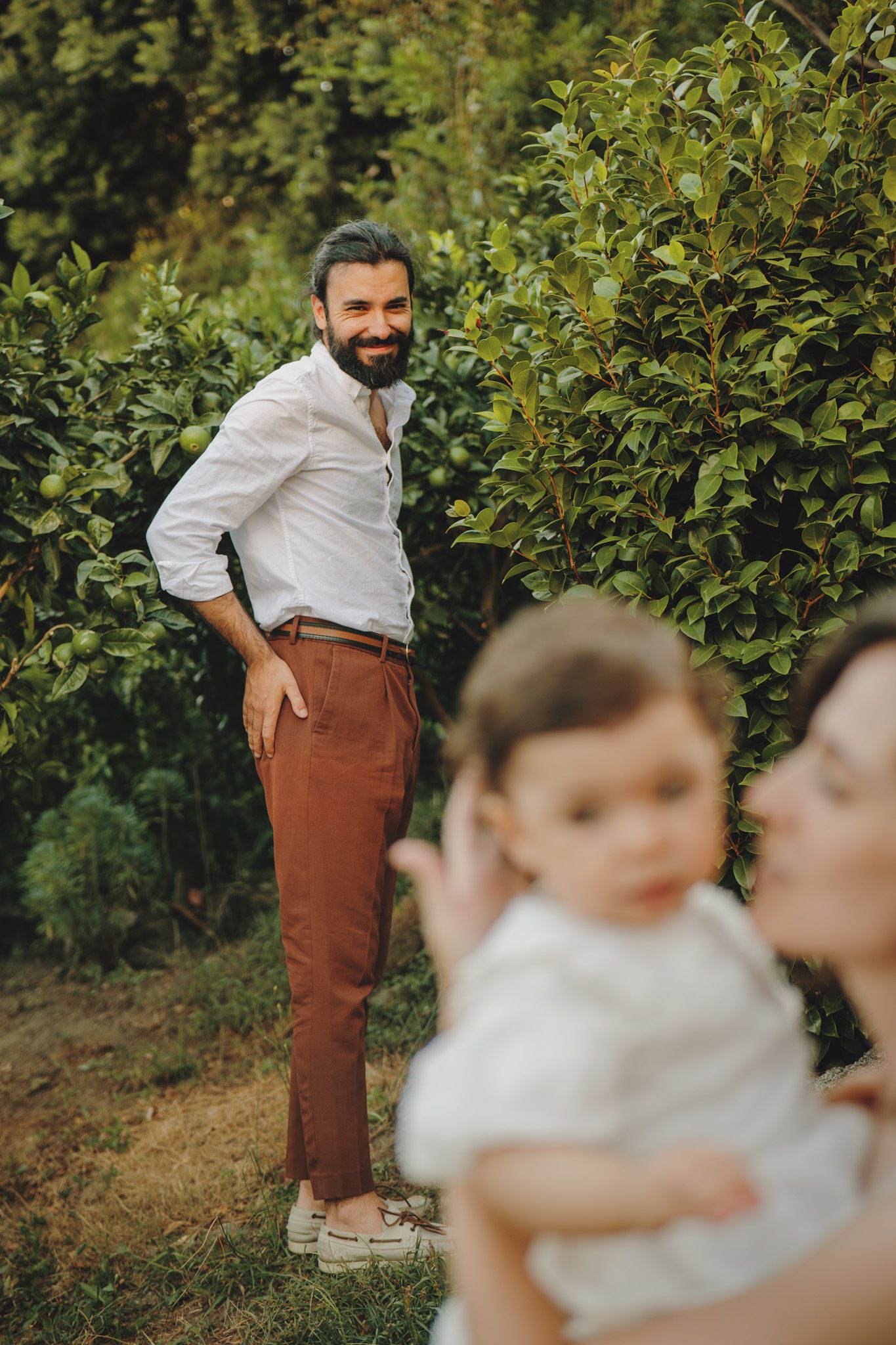 Garden photoshoot featuring brown pants and white clothing against lush green foliage.