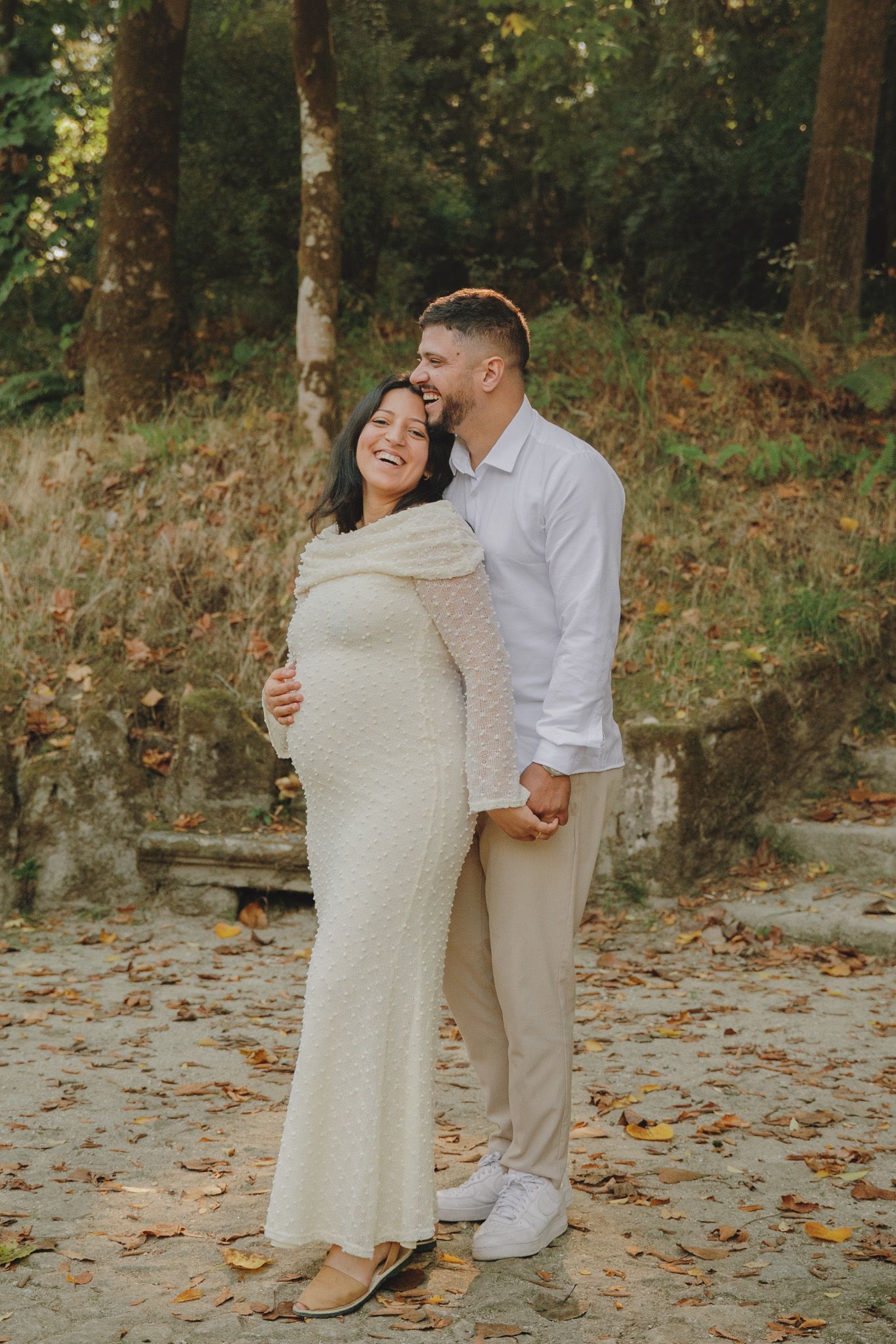 An intimate maternity portrait of a couple in coordinated white and beige outfits.