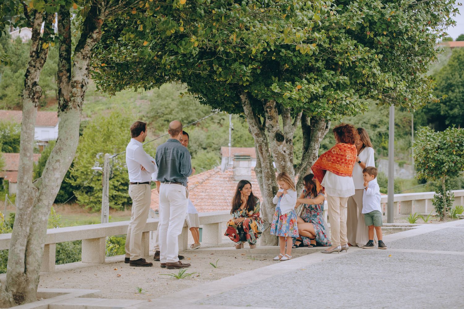 People gathering outdoors under trees on a sunny day.