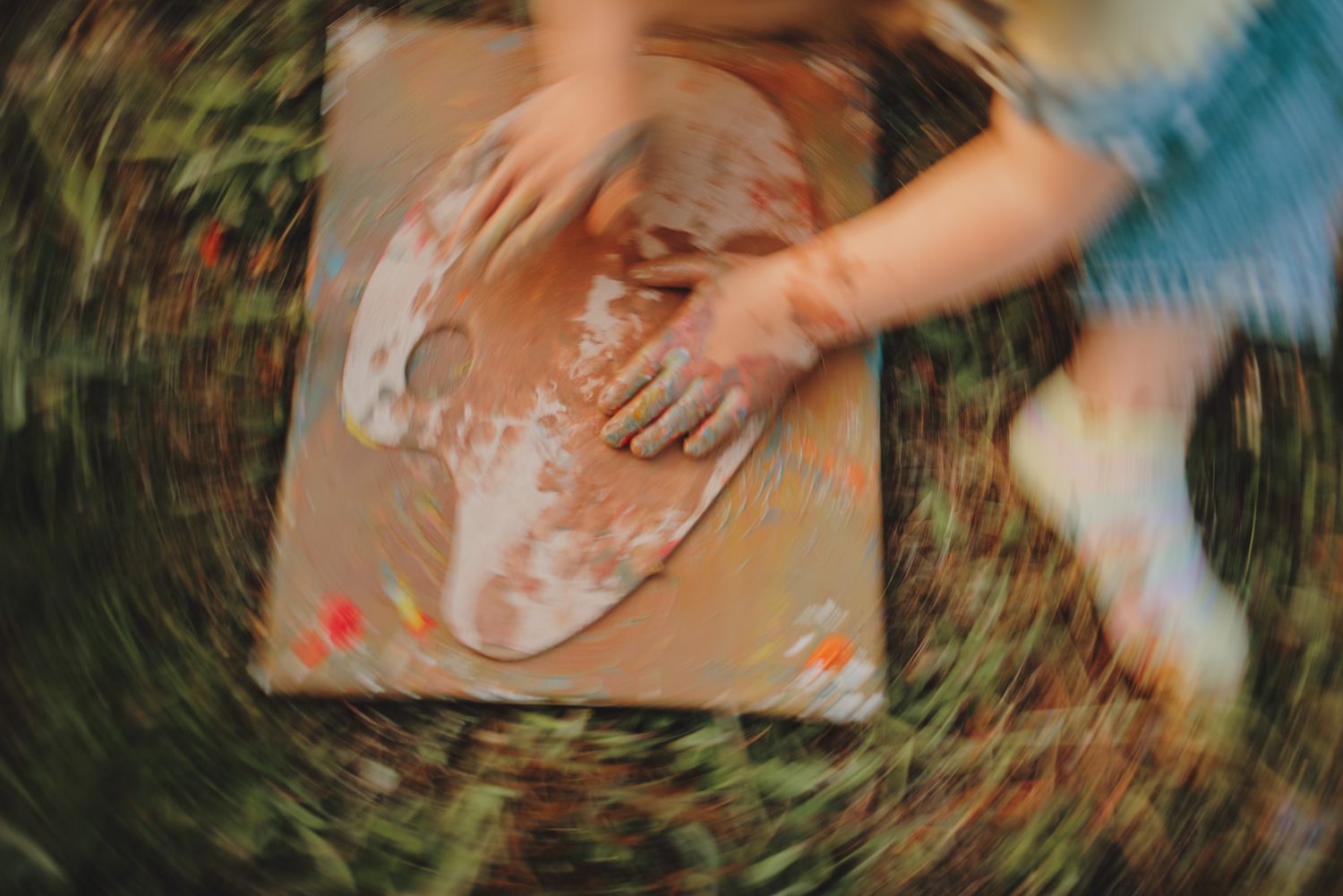 Hands creating art on a canvas outdoors with paint in a blurred motion shot.