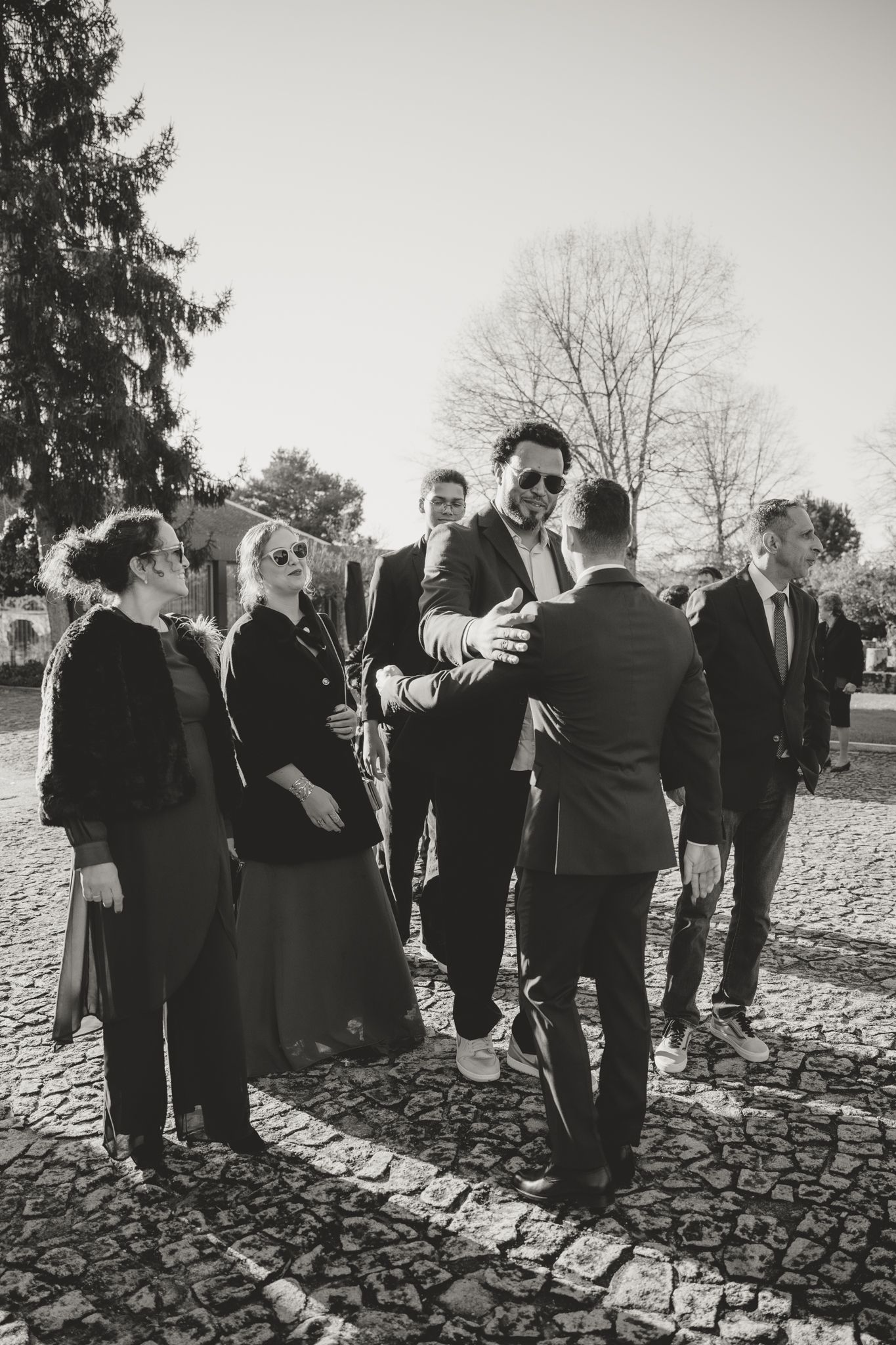 Wedding guests gather outdoors on a cobblestone path during a black and white photography session.