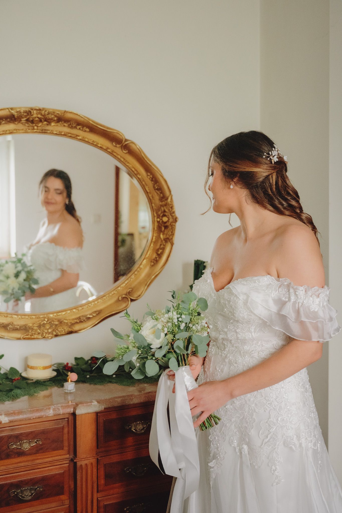 Elegant wedding dress details captured near an ornate gold mirror and wooden furniture.
