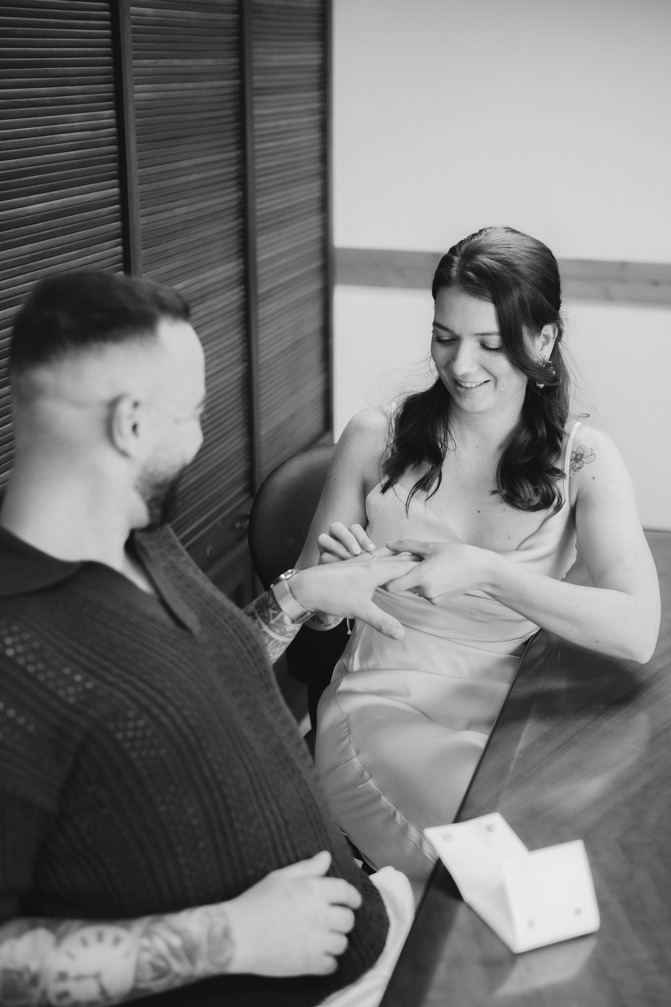 A couple shares an intimate moment while exchanging rings in a black and white photograph.
