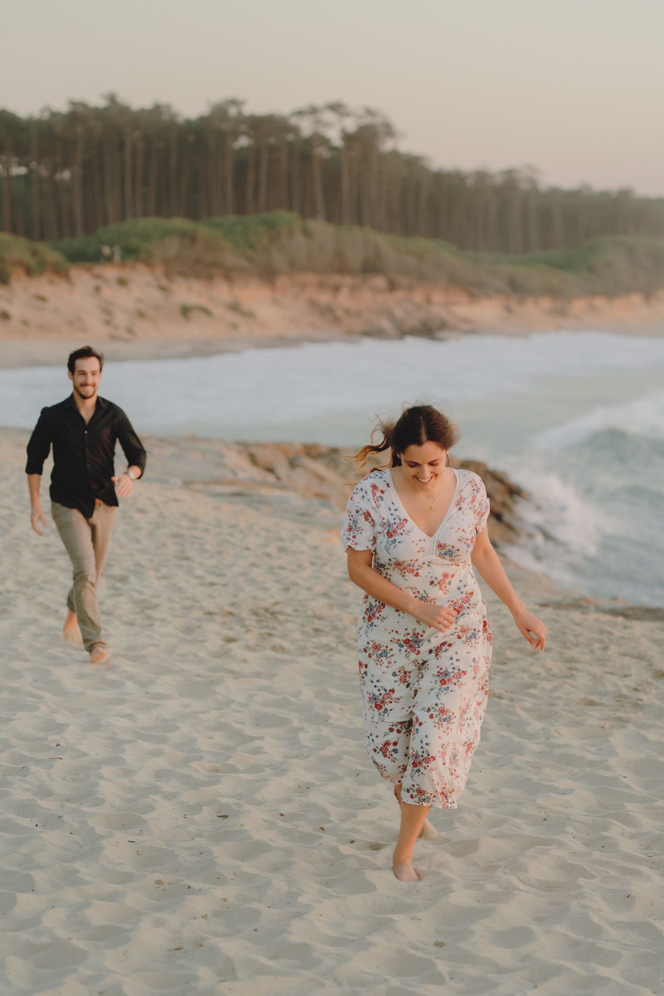 Playful couple chasing each other across sandy beach dunes at dusk.