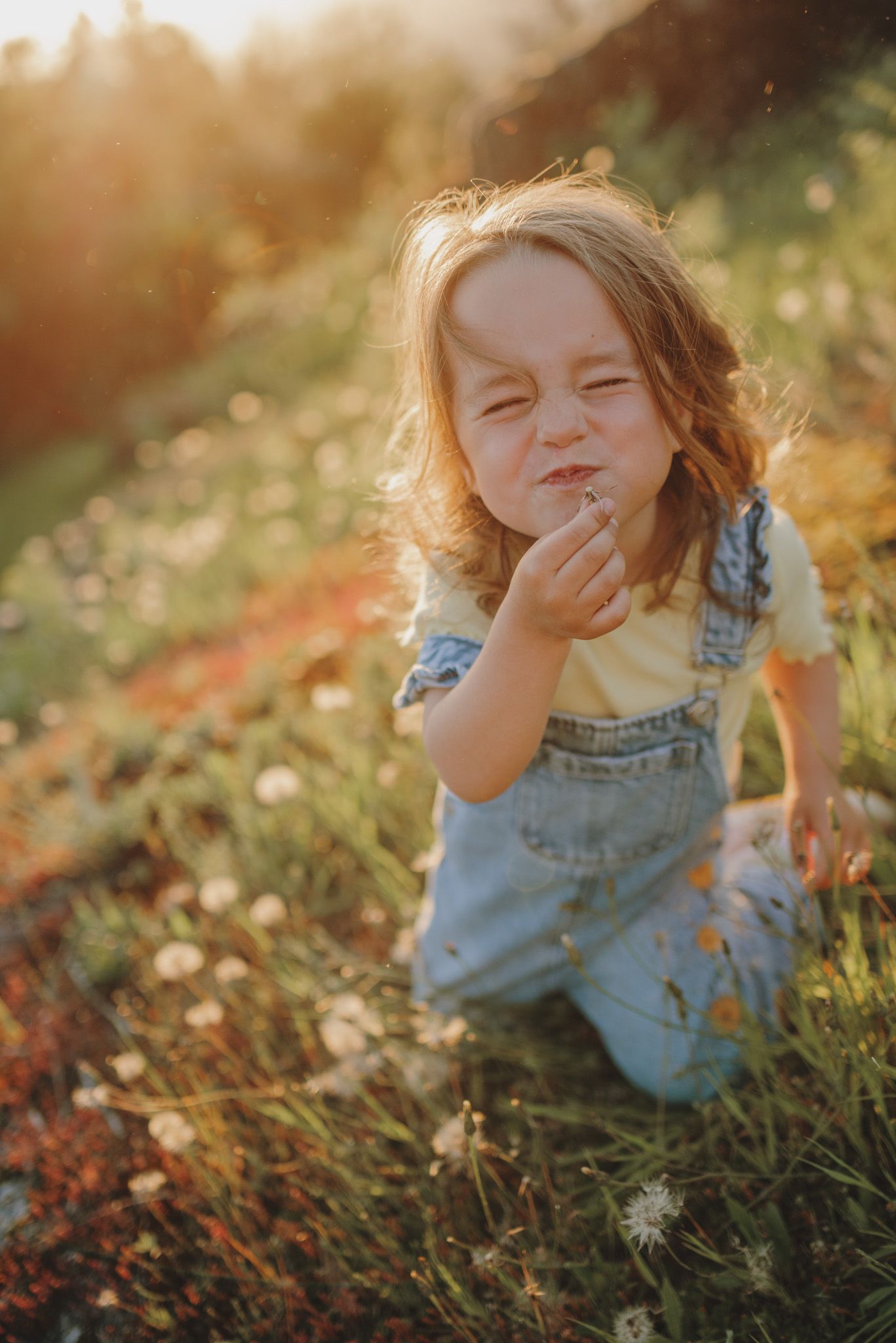 A child laughs while playing in a grassy field during golden hour, wearing denim overalls.