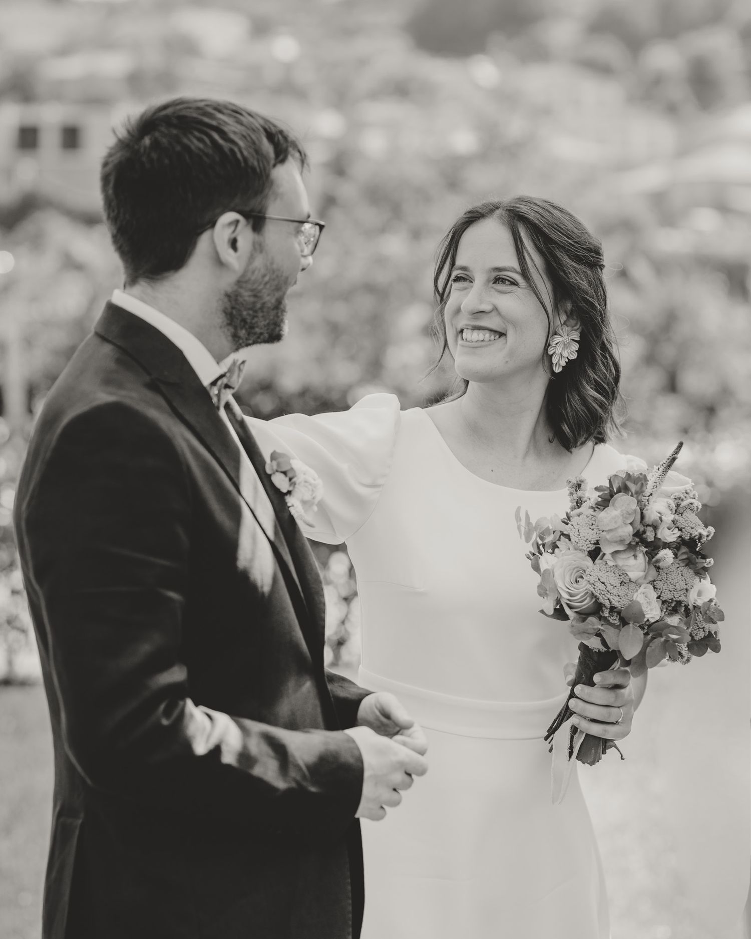 Black and white wedding photo capturing a tender moment with a bouquet on an outdoor deck.
