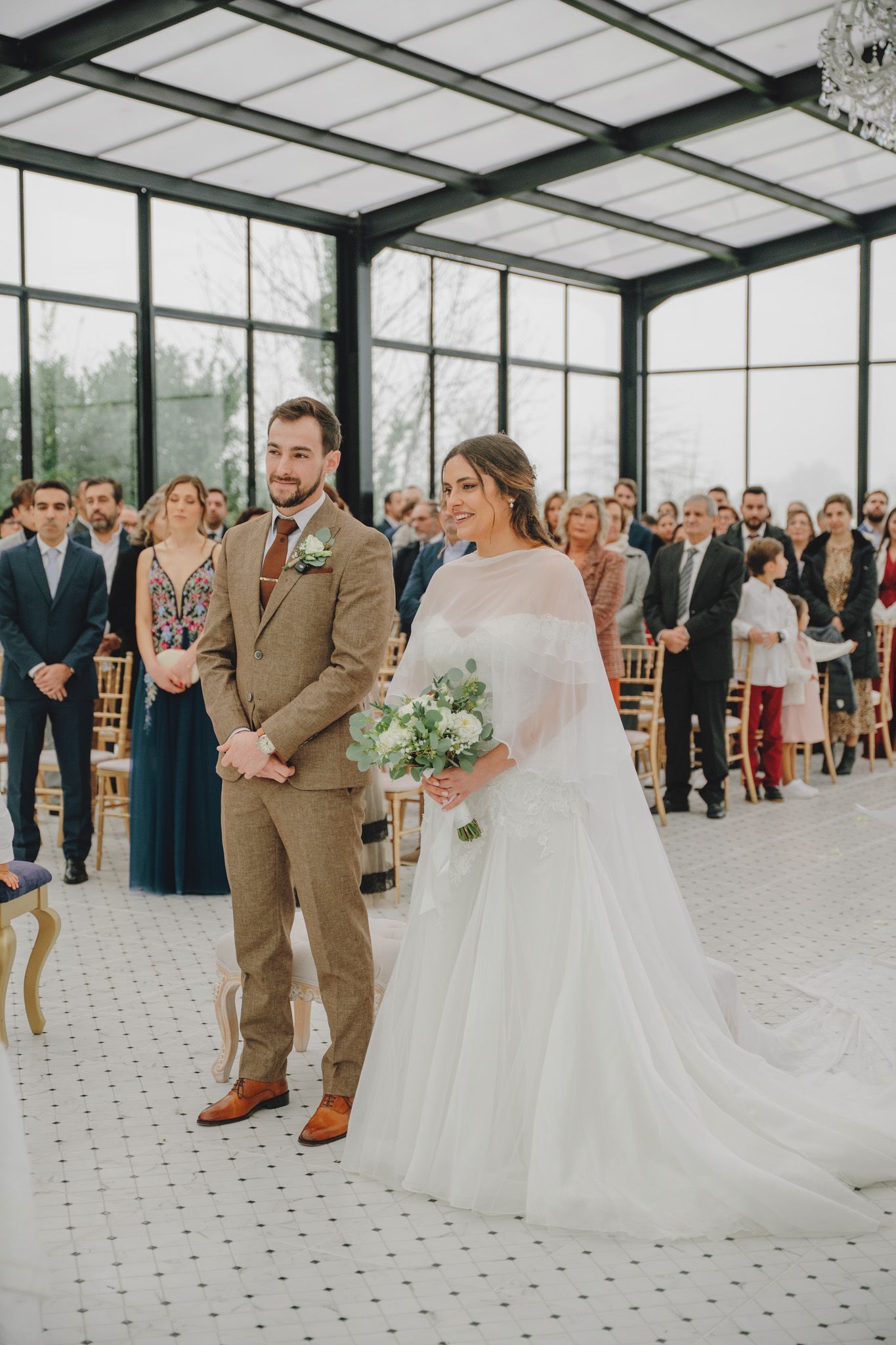 Wedding ceremony in a bright glass-enclosed venue with guests watching the celebration.