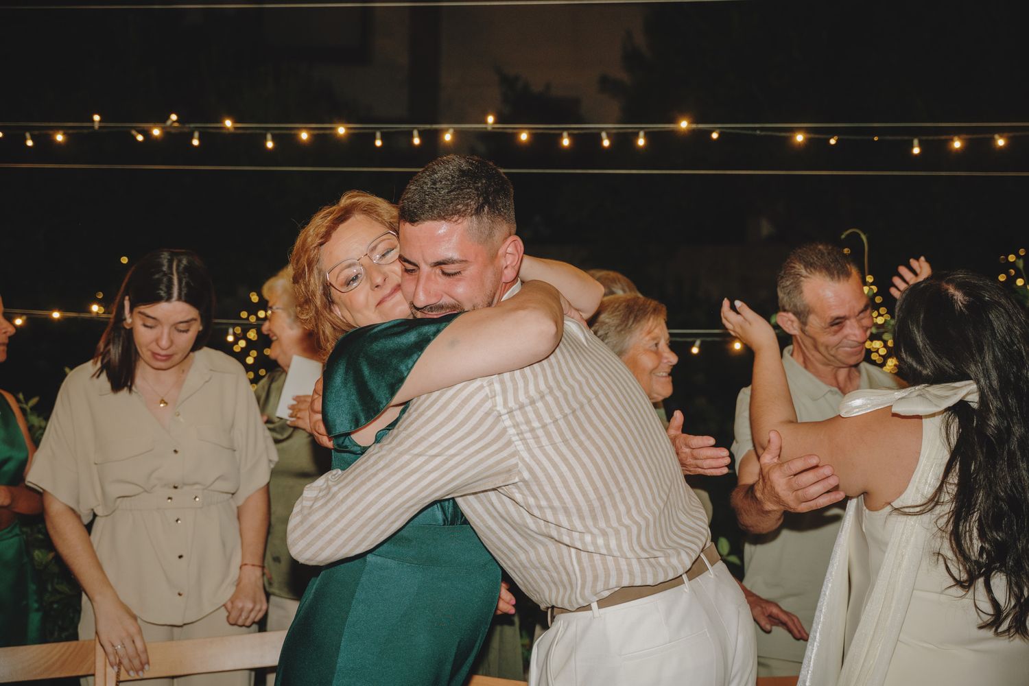 Outdoor evening celebration with guests enjoying drinks under string lights.