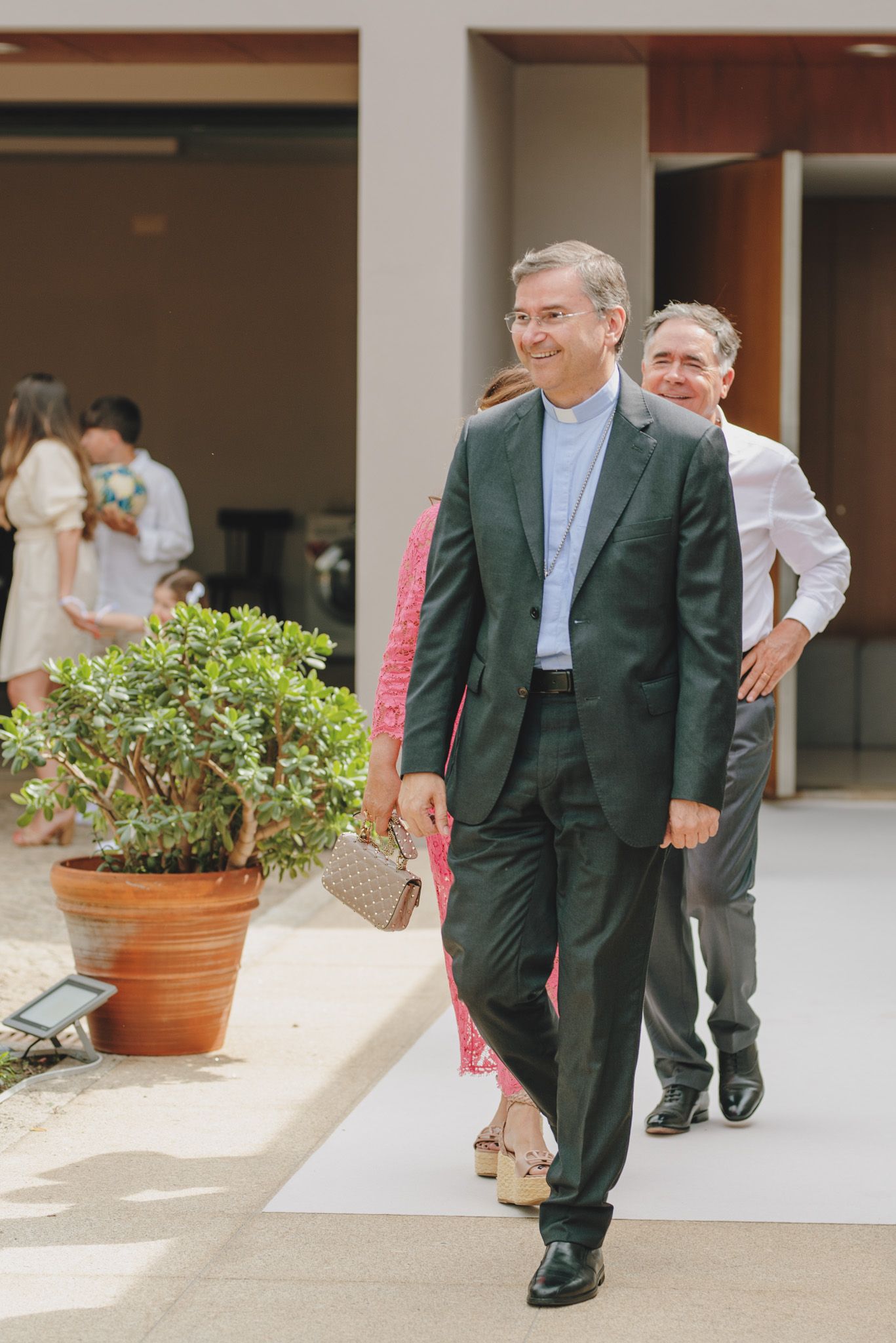 Groomsmen in dark green suits walk together down a pathway at an outdoor venue.