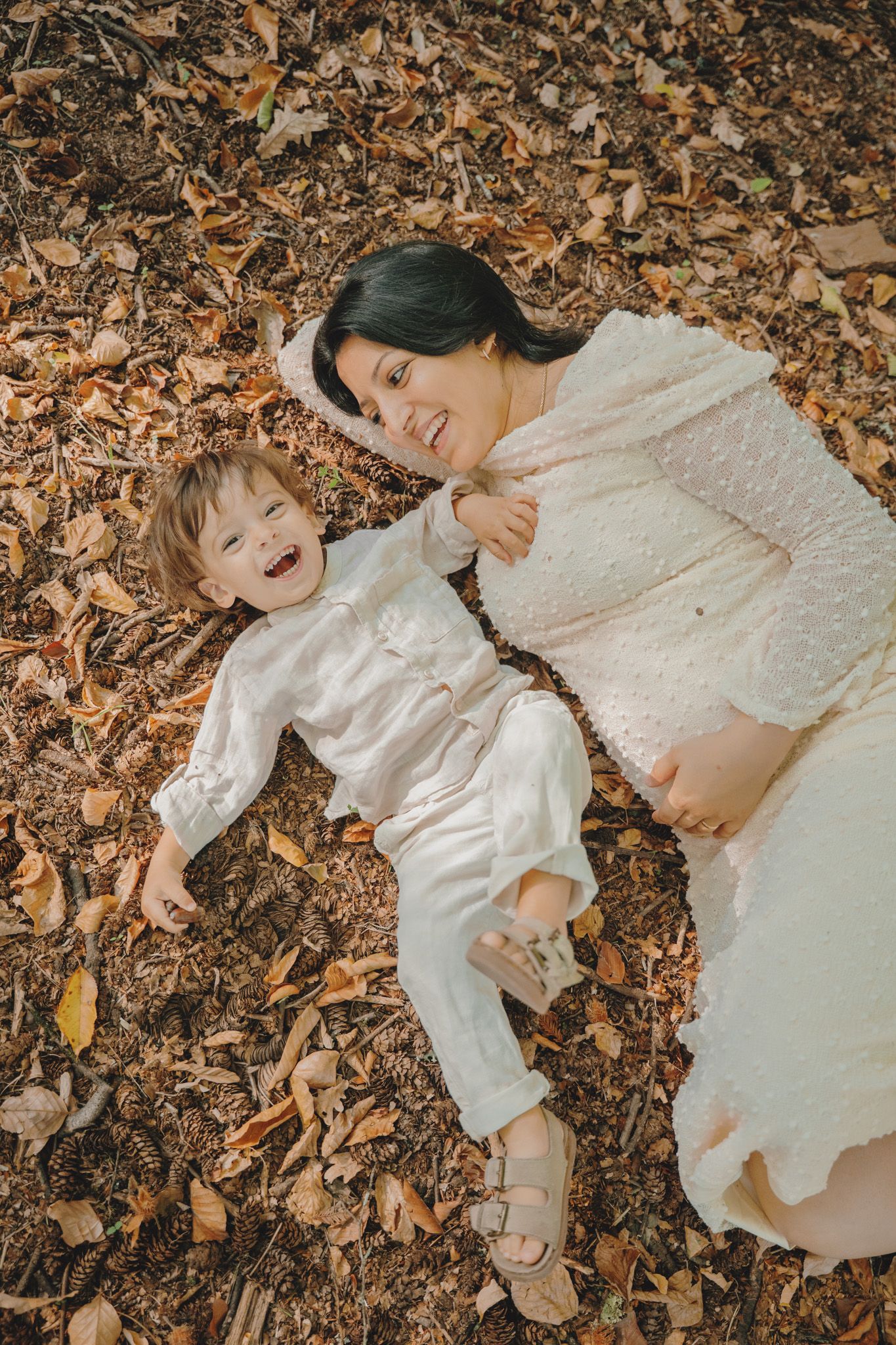 A mother and child lie on autumn leaves sharing a joyful moment together.