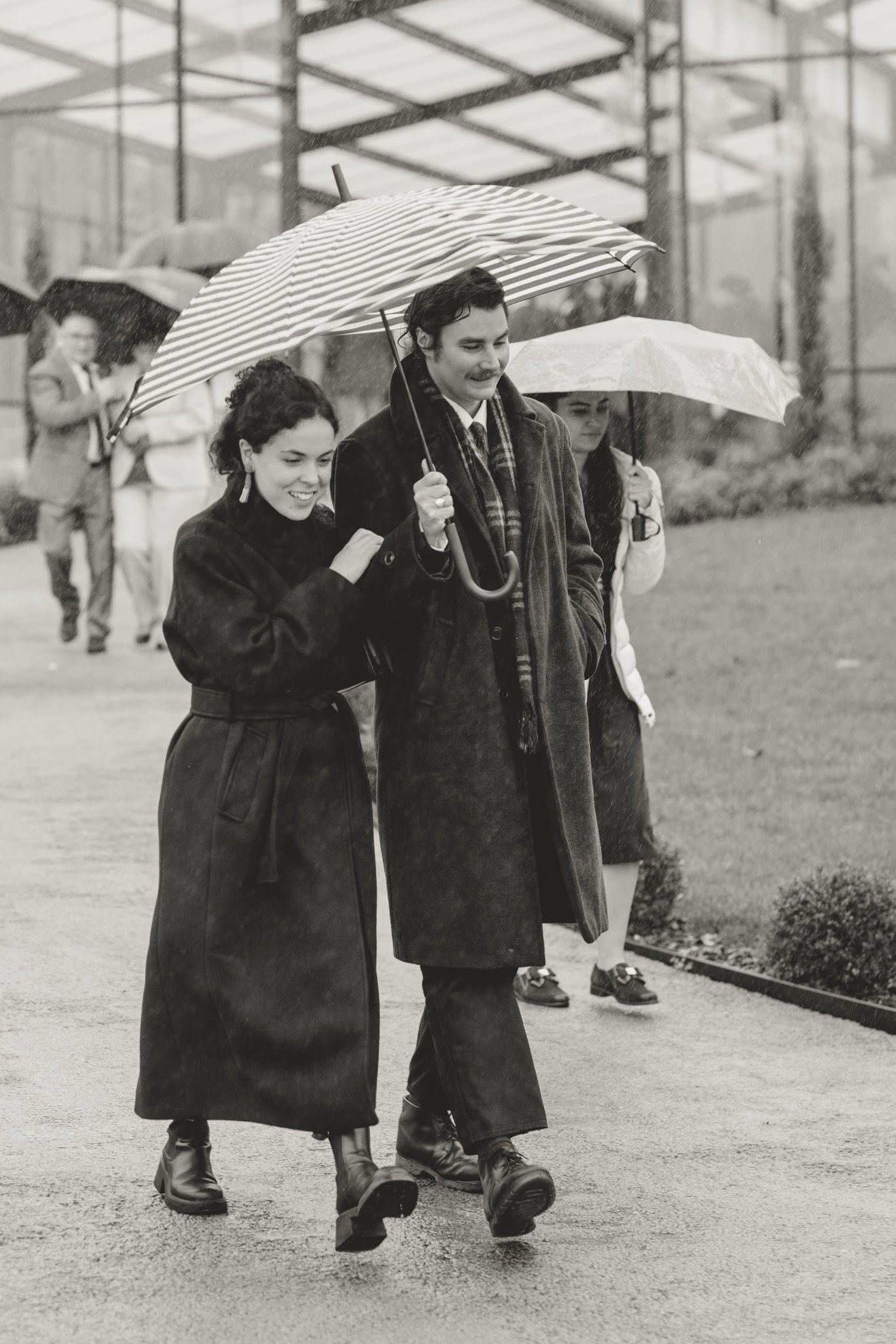 People walking with umbrellas in the rain on a wet path.