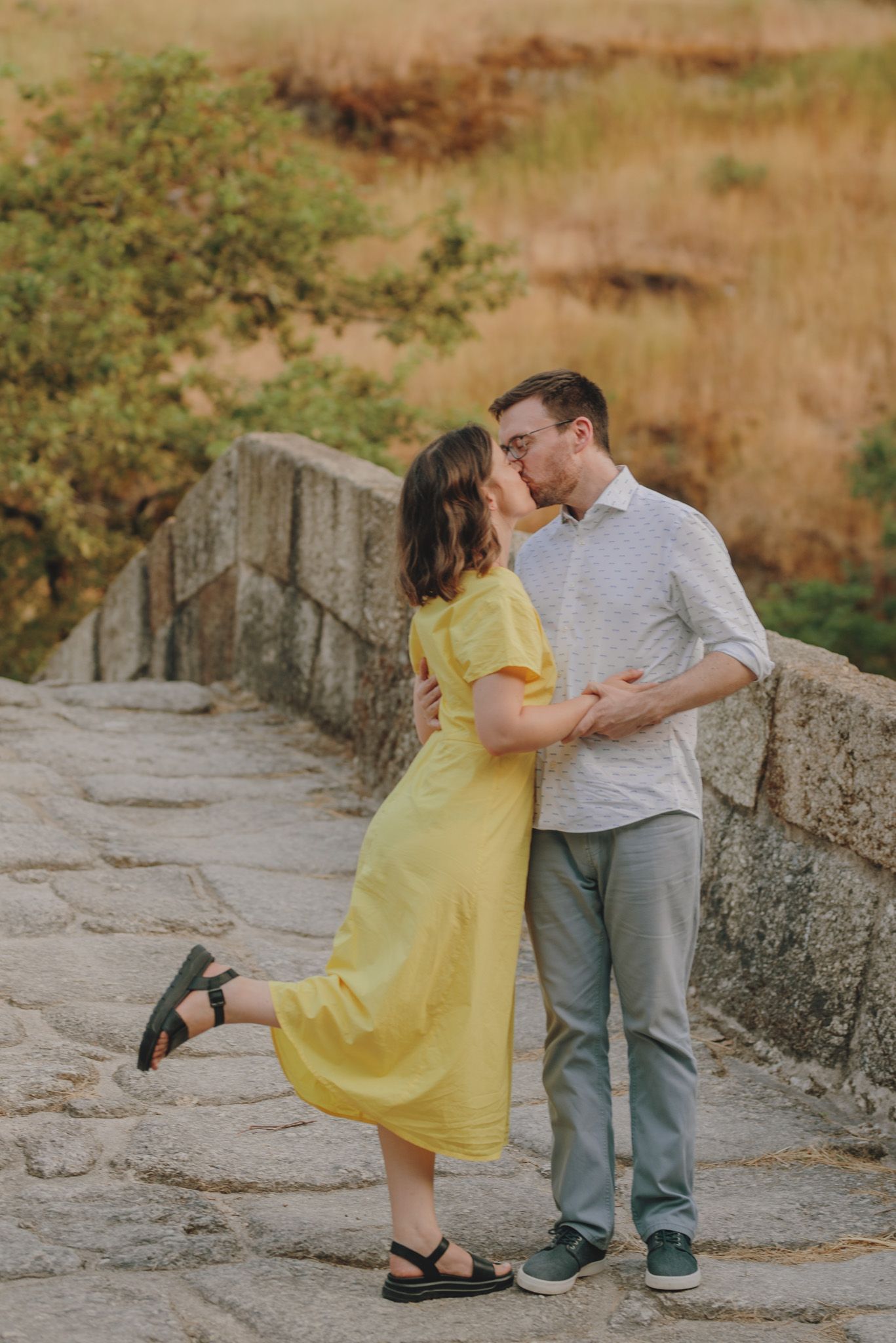 A couple shares a romantic moment on a stone path with a yellow dress adding a pop of color.