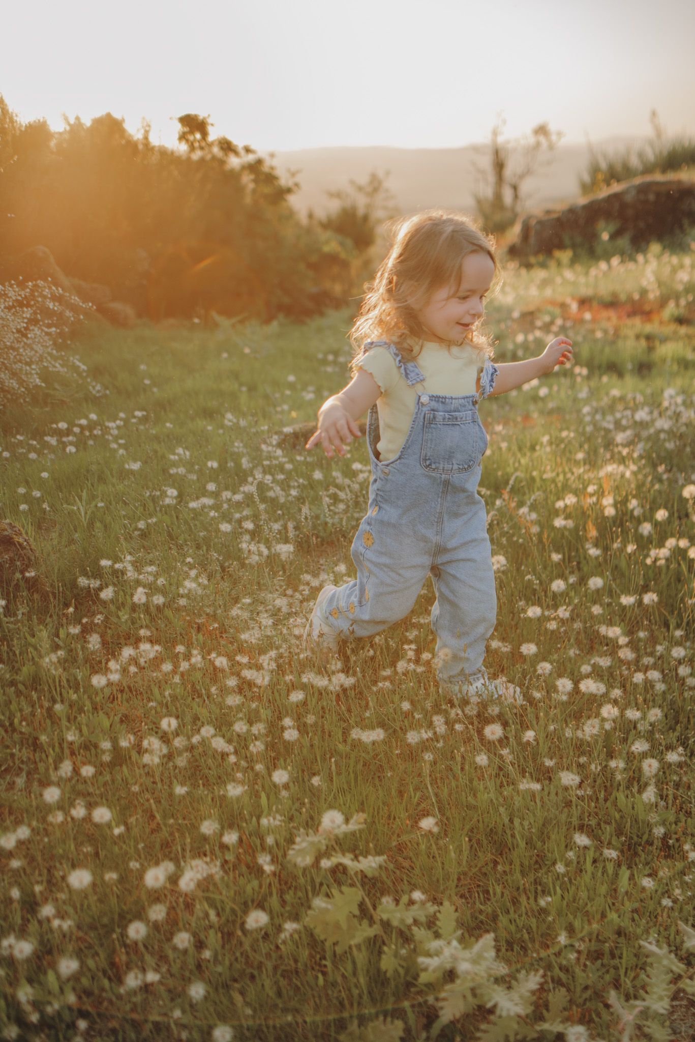 Running through a meadow of dandelions at golden hour in denim overalls.