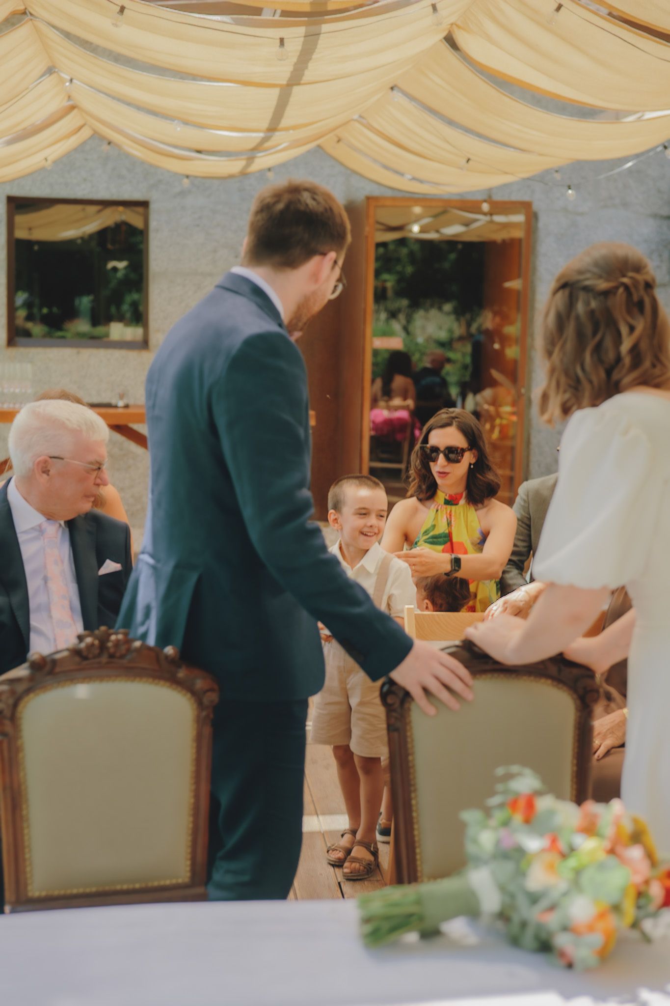 Wedding guests seated at elegant tables under a light fabric canopy during an outdoor reception.