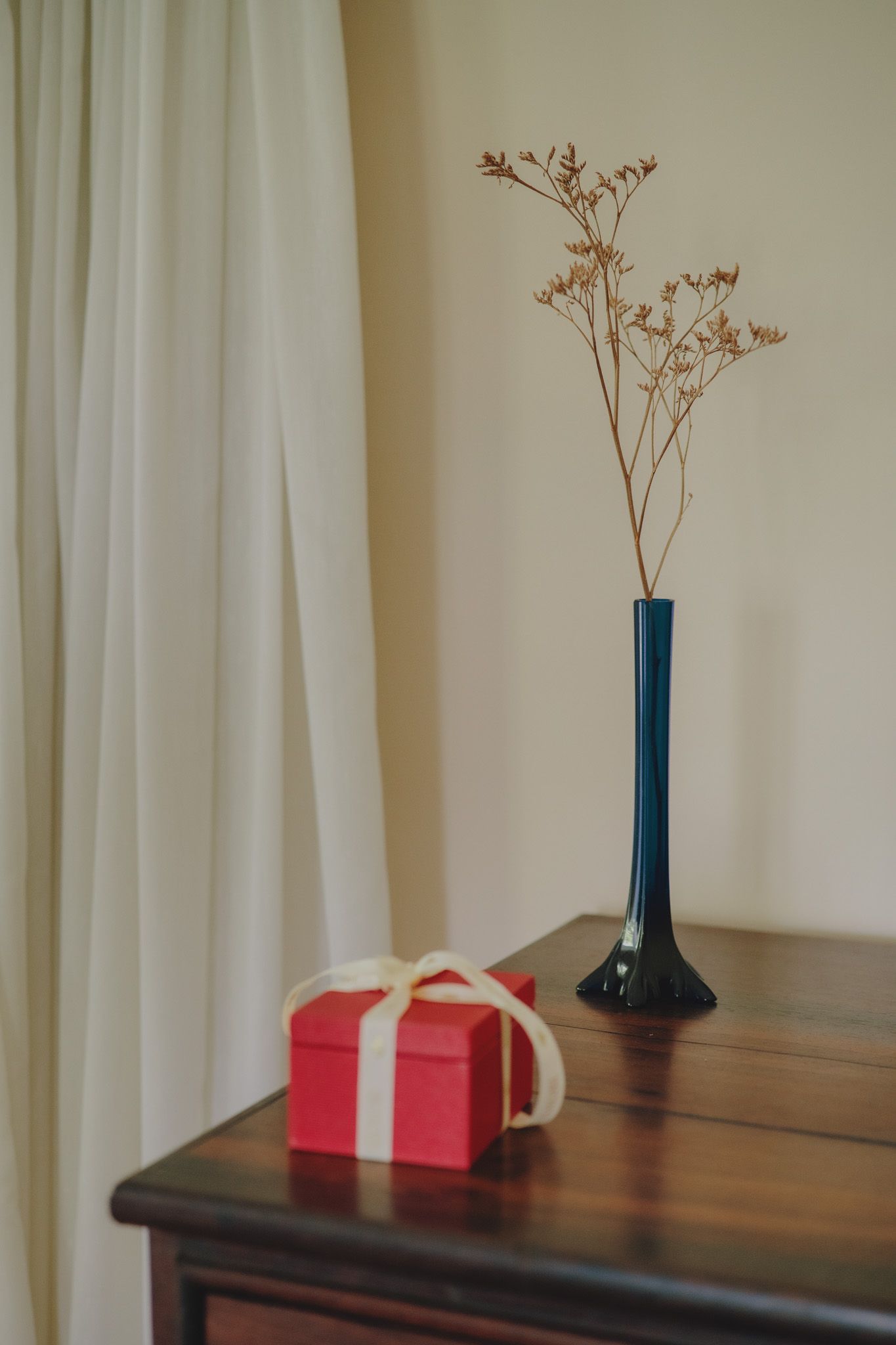 A minimalist still life with a blue vase and pink gift box on a wooden surface against a white wall.