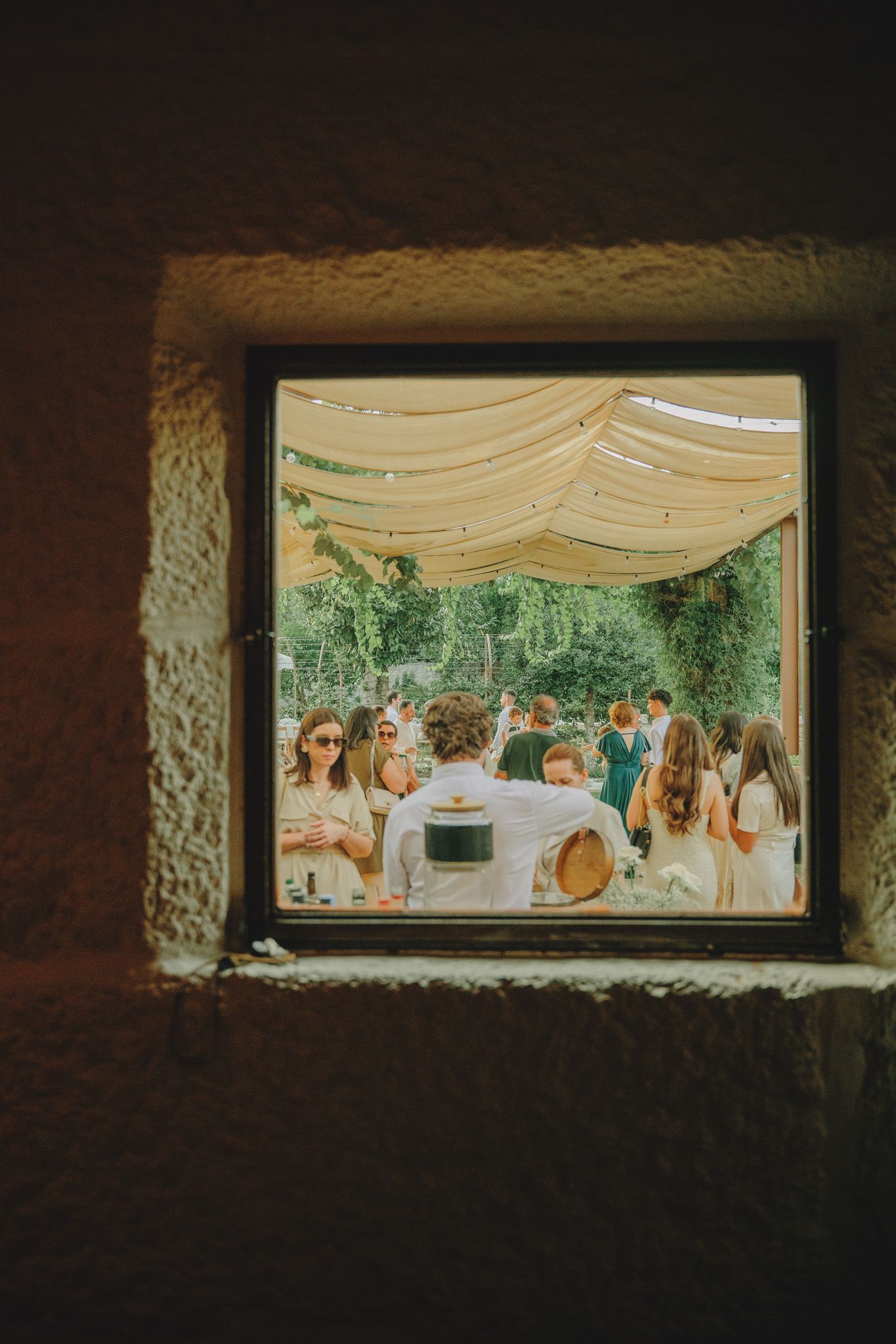 View through a window frame of an elegant outdoor wedding reception under white draping.