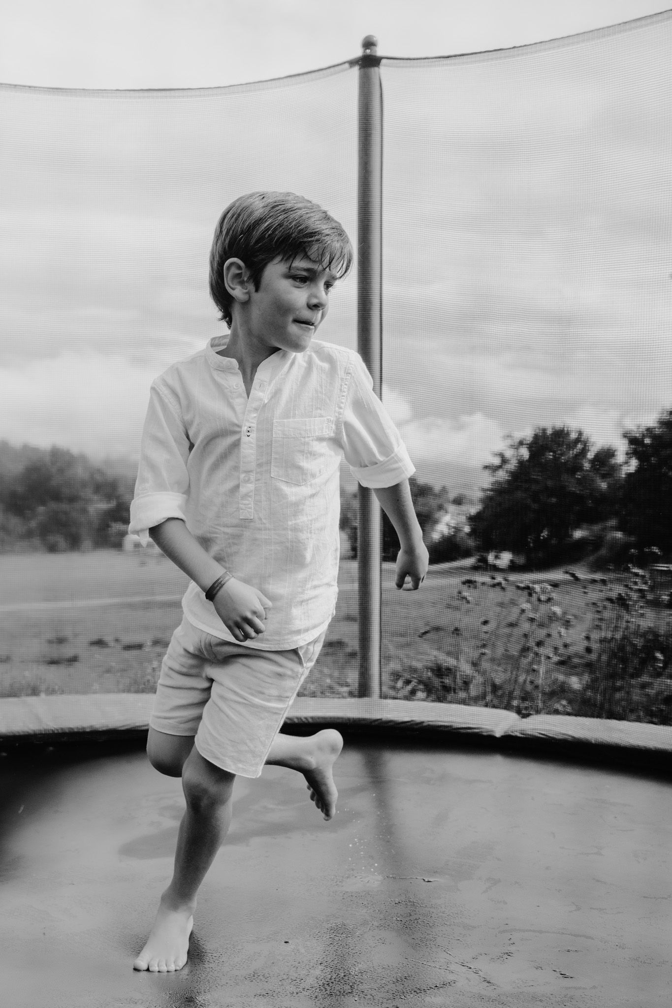 Black and white sequence of a child jumping and playing on a wet trampoline on an overcast day.