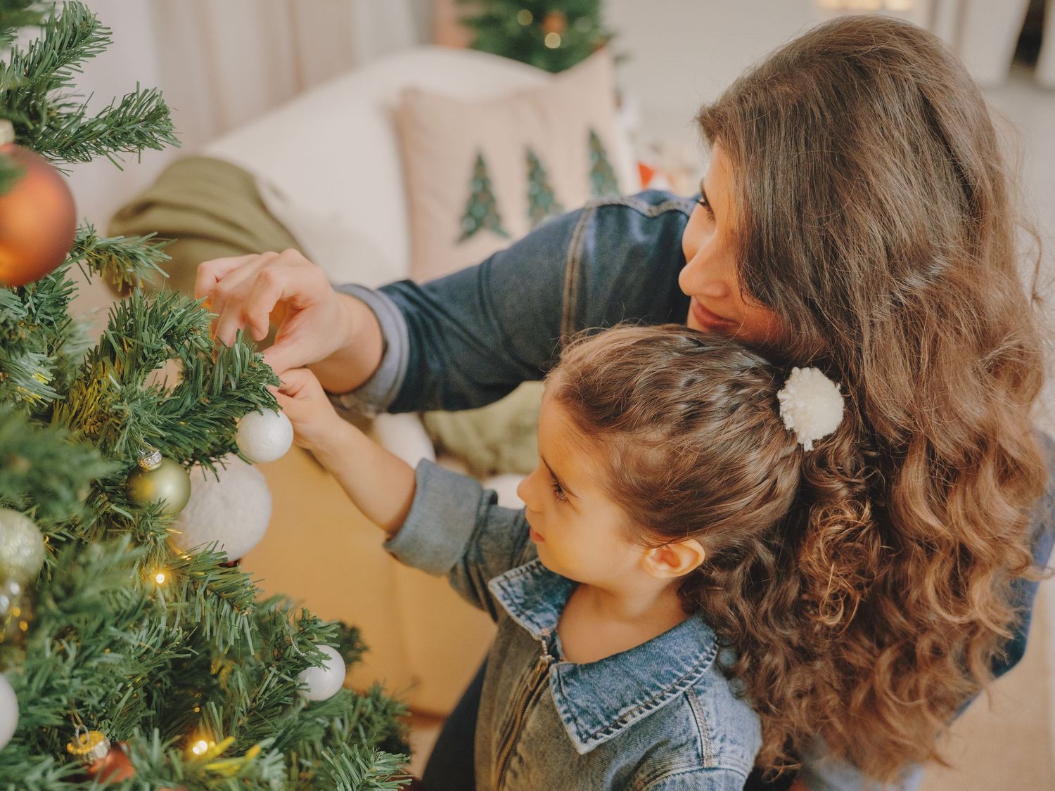 Mother and child decorating a Christmas tree together with ornaments in a cozy living room.