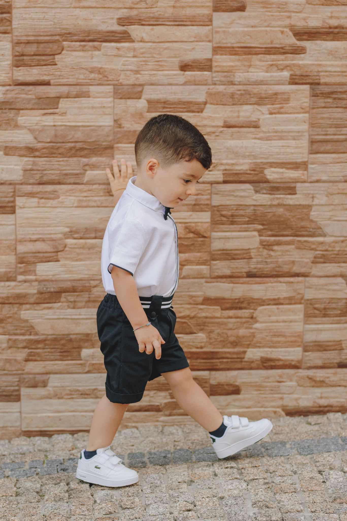 Child in white shirt and dark shorts jumping along stone wall in sequence of action shots showing movement.