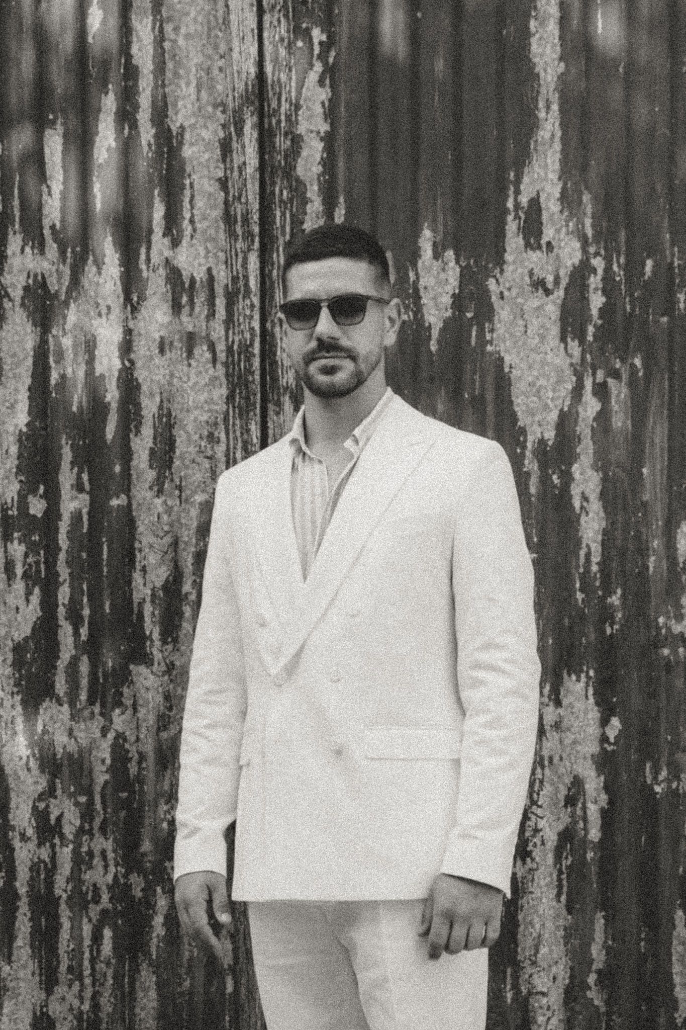 A person in white clothing stands against a weathered wooden door.