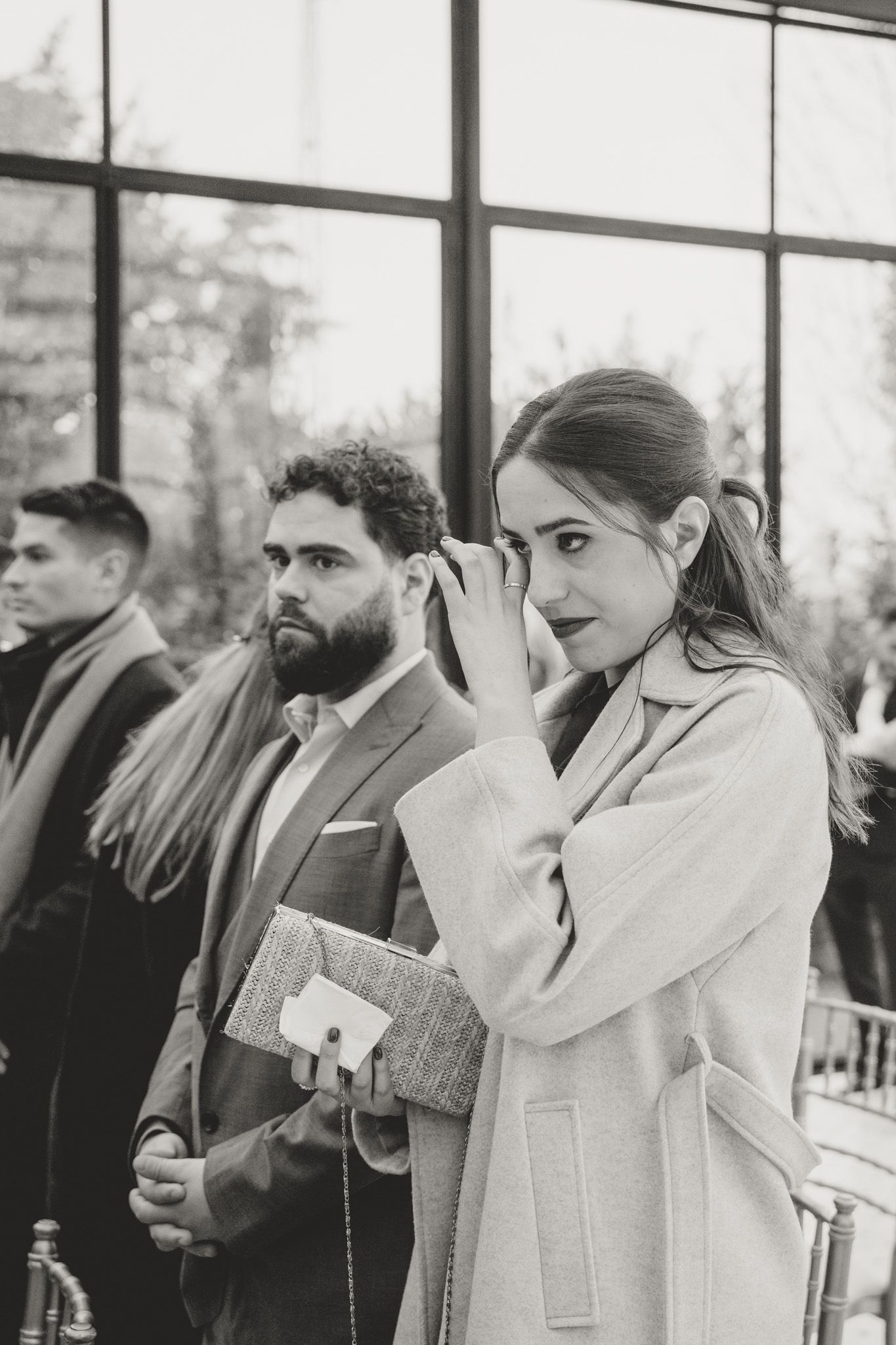 Wedding guests in formal attire watch emotionally during an indoor ceremony.