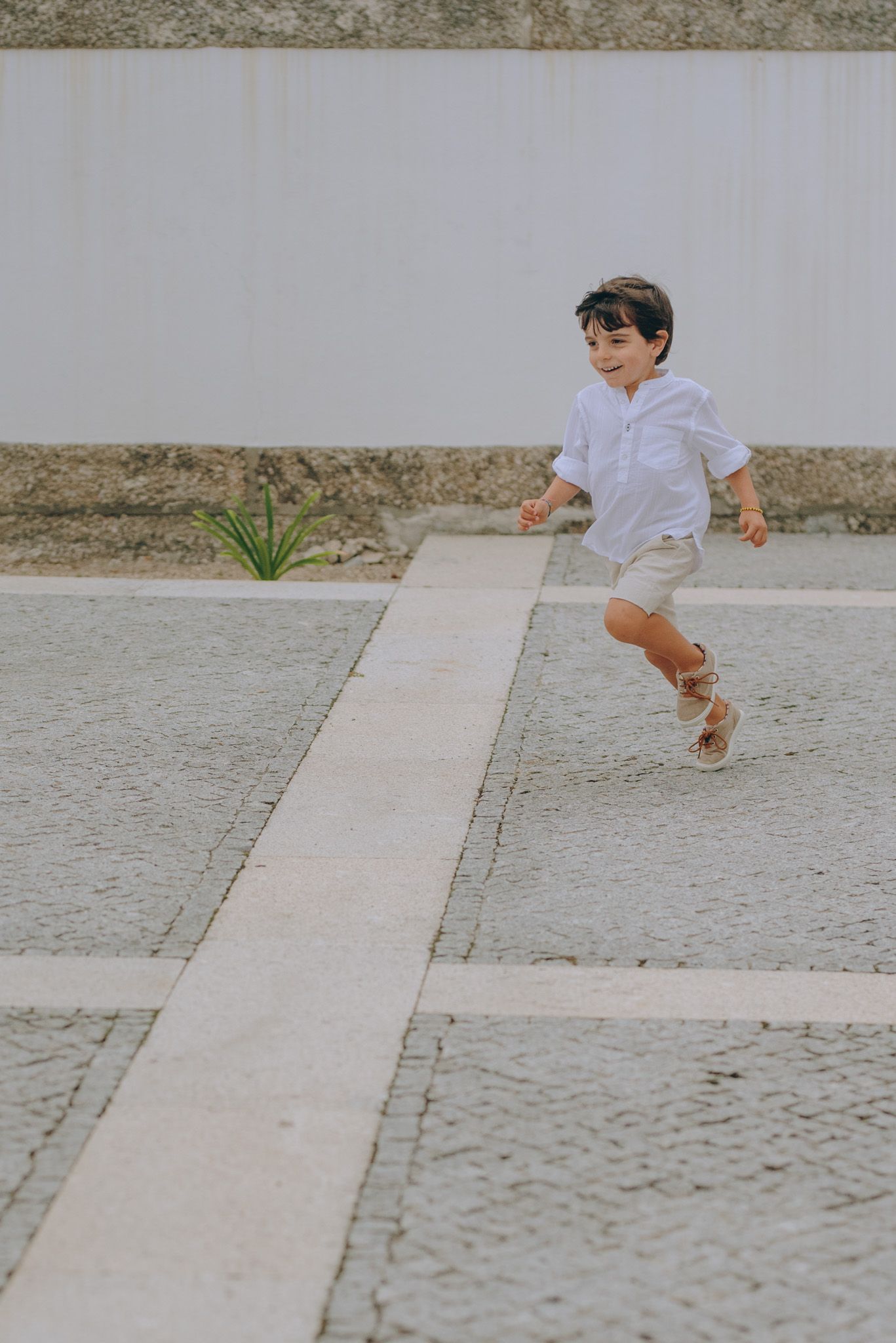 Child in white clothing jumping across stone pathways.